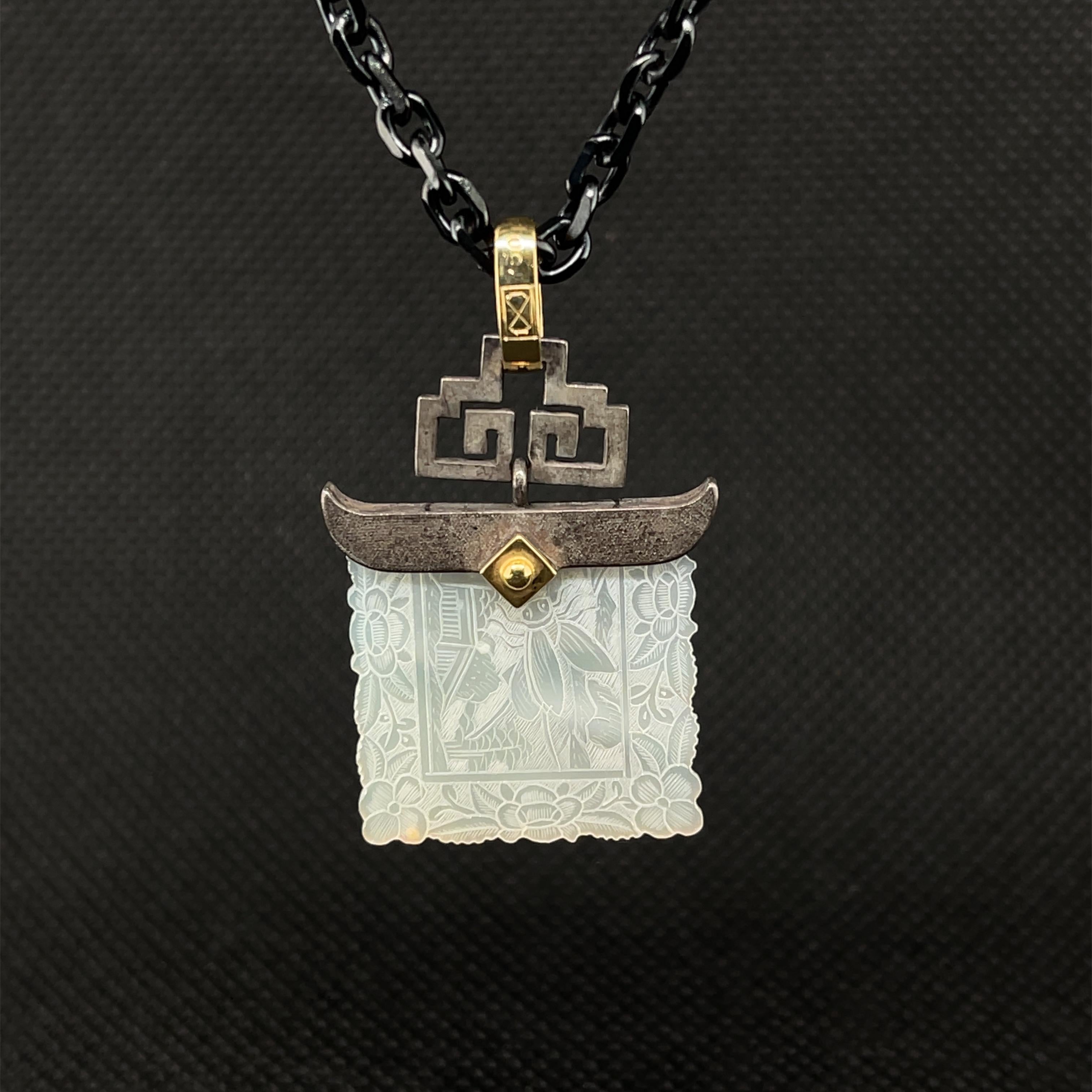 This pretty pendant features an antique, mother-of-pearl Chinese gambling counter dating back to the 18th Century. The square gaming counter with scalloped edges is set in a striking blackened silver setting with curved ends and a design that is