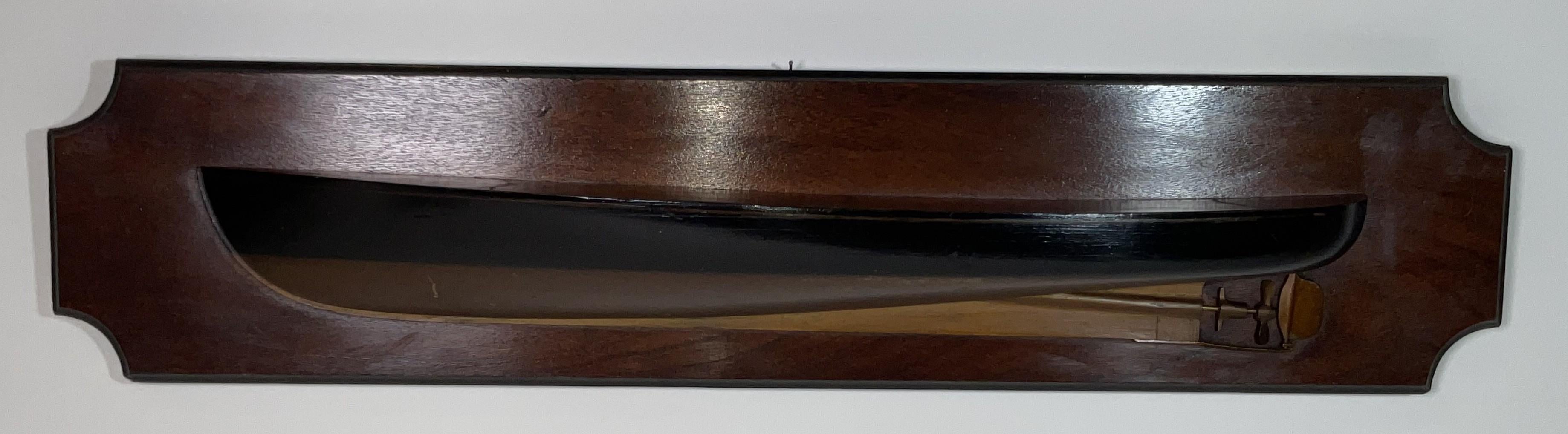 Late nineteenth century half model of a motorized launch, circa 1890. The carved hull is painted black above the waterline and gold below. Fitted with a drive shaft and prop. Mounted to a hardwood backboard.

Weight:    5 lbs.
Overall Dimensions:   