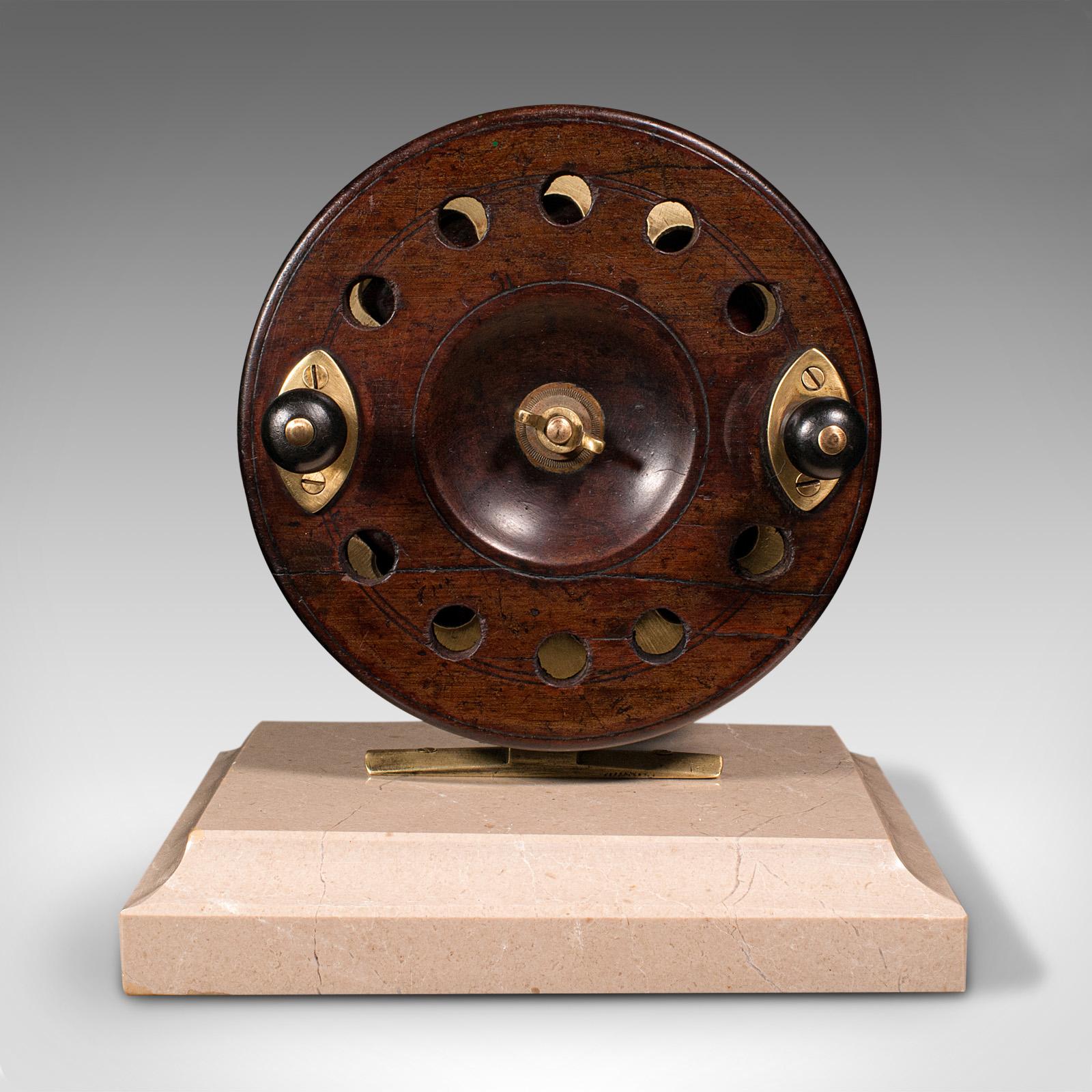 This is an antique mounted fishing reel. An English, mahogany and brass reel of sporting decorative interest and mounted on a travertine base, dating to the late Victorian period and later, circa 1900.

Of great appeal to the keen fisherman for