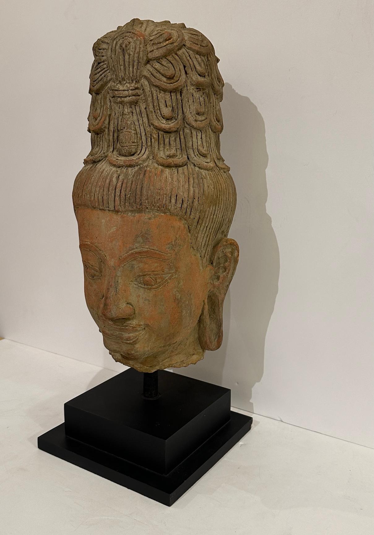 Una scultura in terracotta di un bodhisattva montata successivamente su una base in legno laminato.