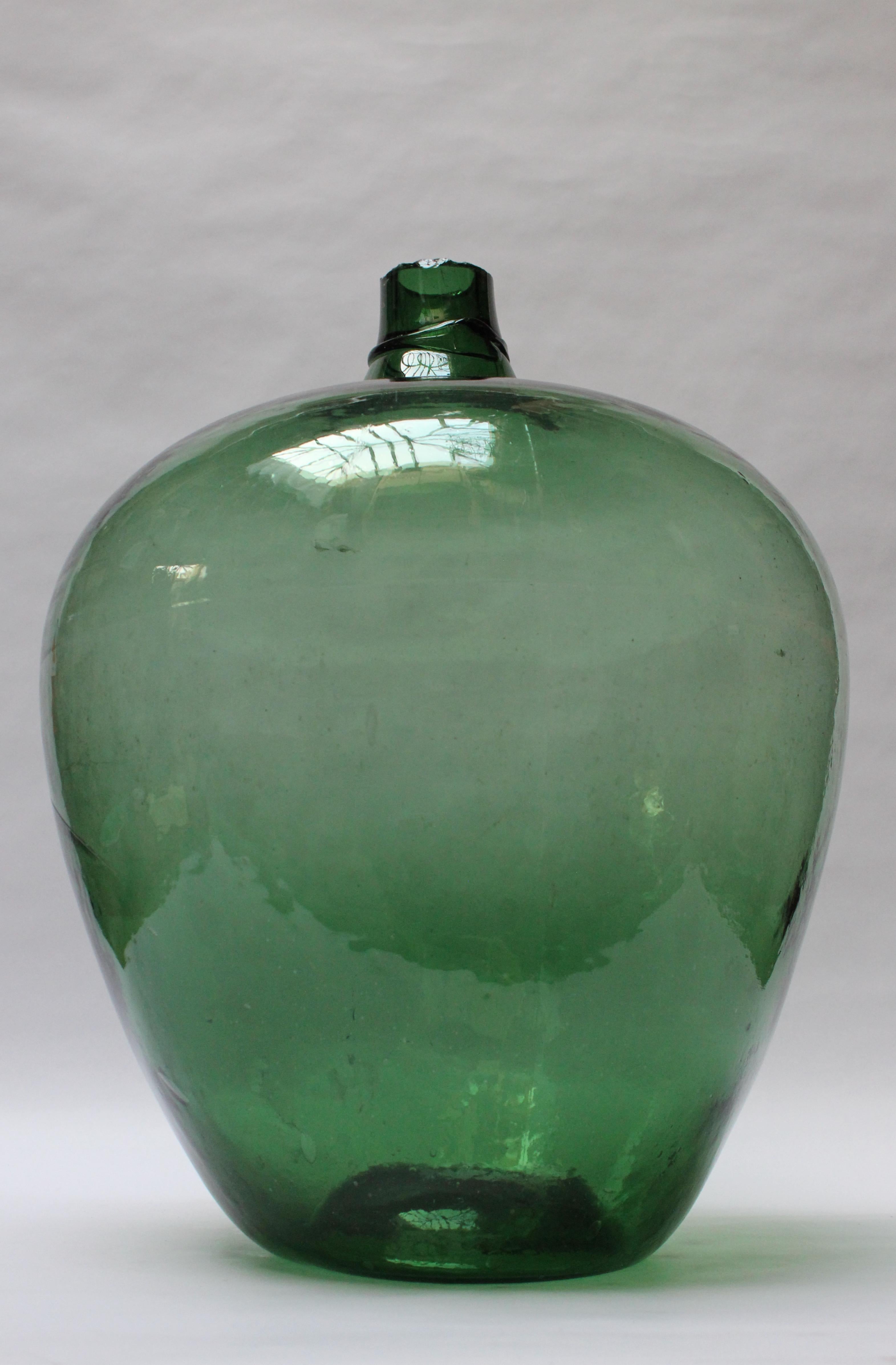 Graceful antique French demijohn / carboy originally used for transporting wine (ca. early 19th Century, France). Composed of mouth blown glass with emerald hue exhibiting trapped air bubbles within the glass itself with a sheared lip and applied
