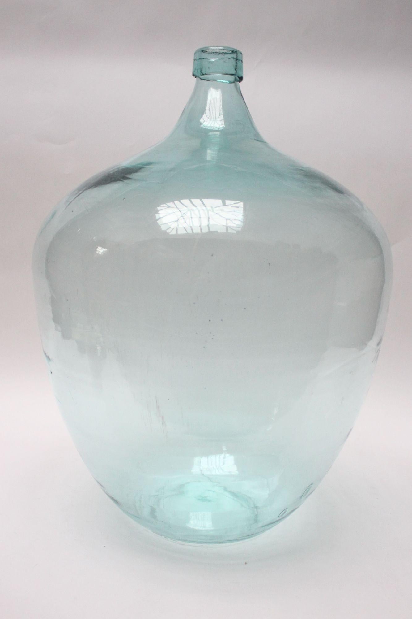 Antique French demijohn/carboy originally used for transporting wine (ca. early 20th Century, France).
Composed of mouth blown glass with ice blue hue exhibiting trapped air bubbles within the glass itself with an applied ring. Unique, stout form,