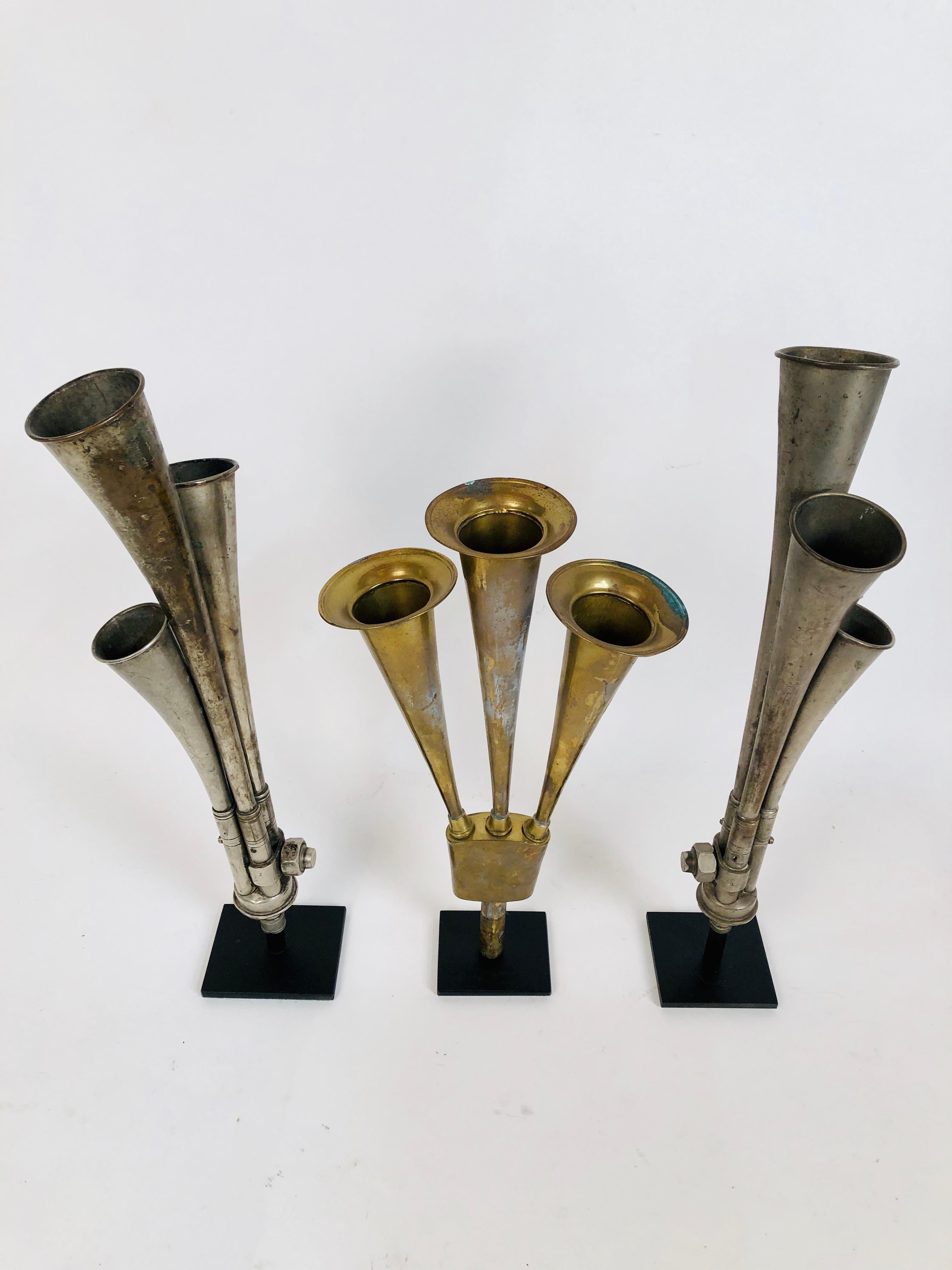 A collection of 3 antique multi tone car horns. All three mounted on custom made stands. One is brass and two are chrome-plated steel. They measure 14