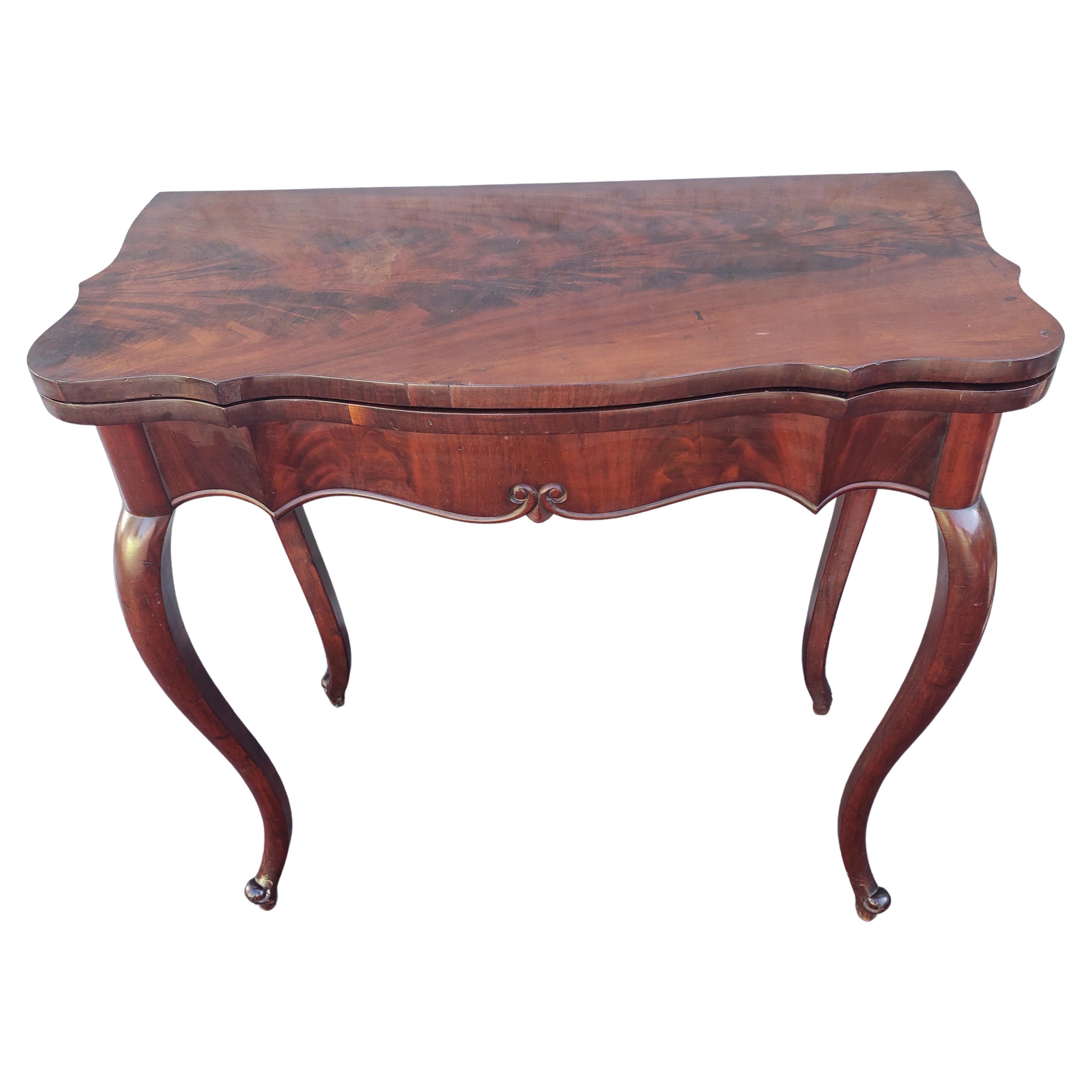 This beautifully proportioned table has a flip top in flame mahogany . Once opened, a playing surface of green baize, surrounded by well kept flame mahogany, is revealed. The gently scalloped apron flows attractively into gently curved cabriole