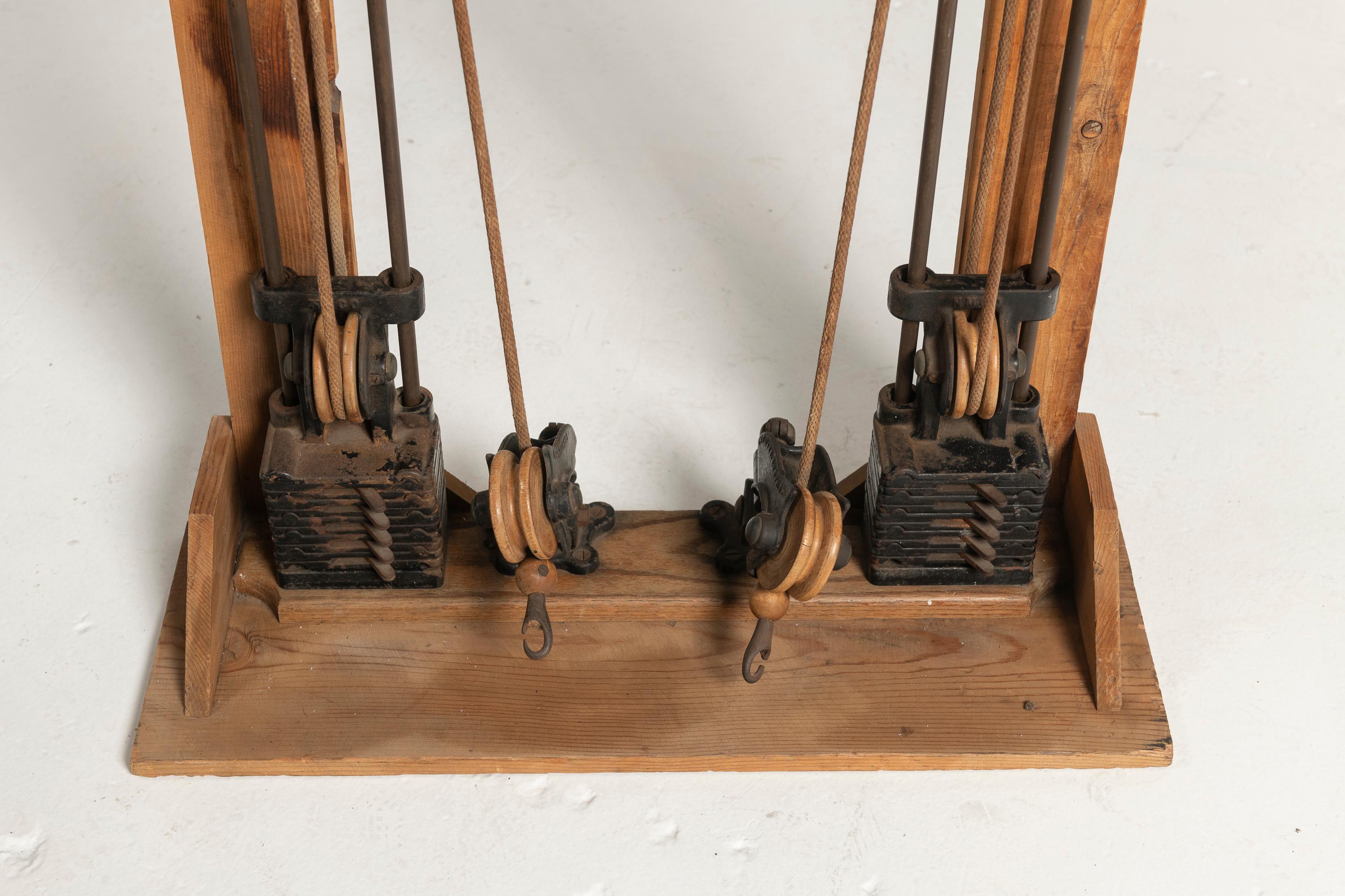 Antike, an der Wand montierte gusseiserne Machine für den Fitnessbereich. Dieses frühe Trainingsgerät, das für das Schulter- und Armtraining konzipiert ist, verfügt über robuste hölzerne Montageplatten und langlebige gusseiserne Umlenkrollen. Die