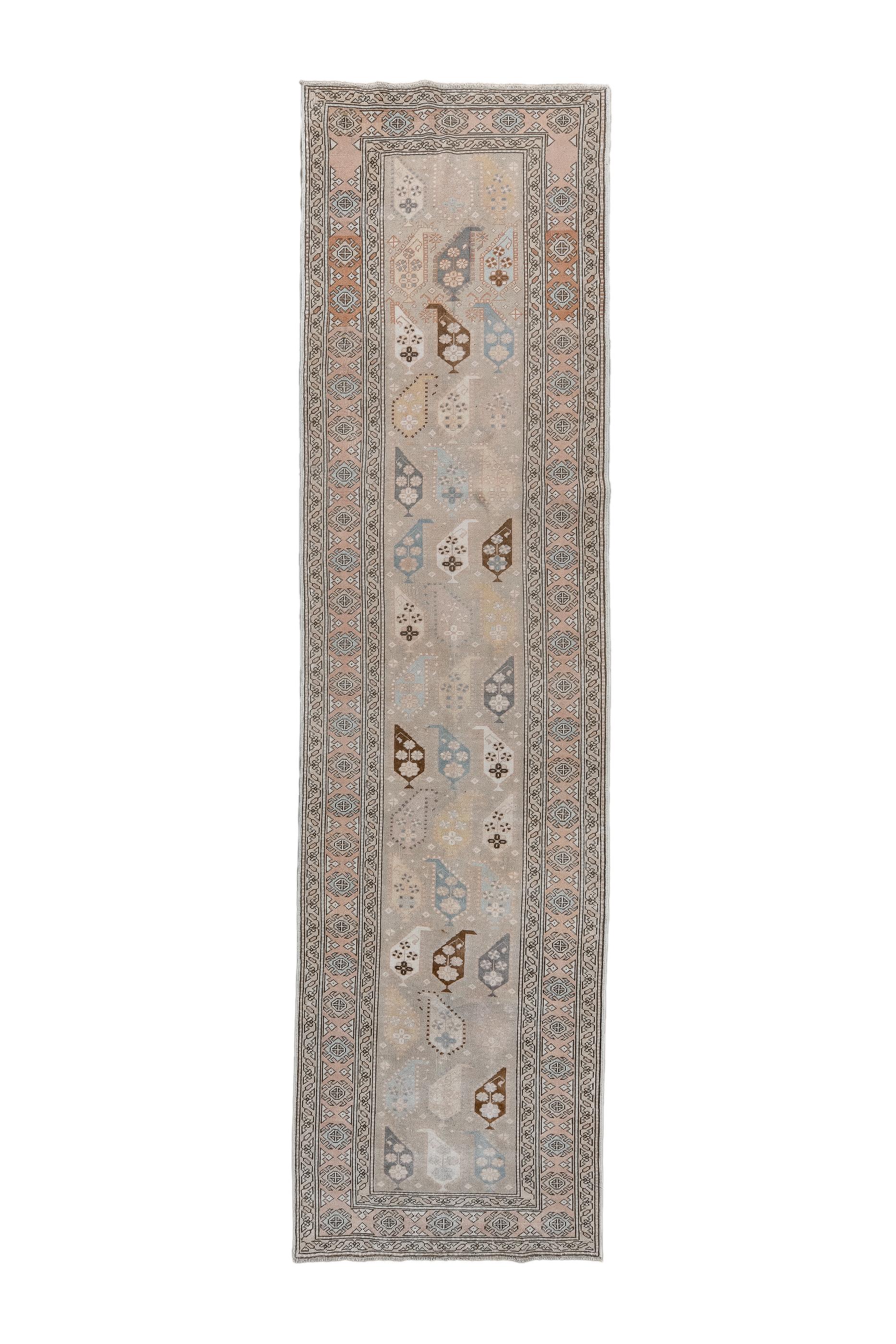 This usefully narrow kenare (runner) shows a traditional, ever-popular design of cascading, upright, stylised and footed botehs on a light ground. Geometric main border of rosettes, brackets, and triangular fillers. Generally reduced tonality with