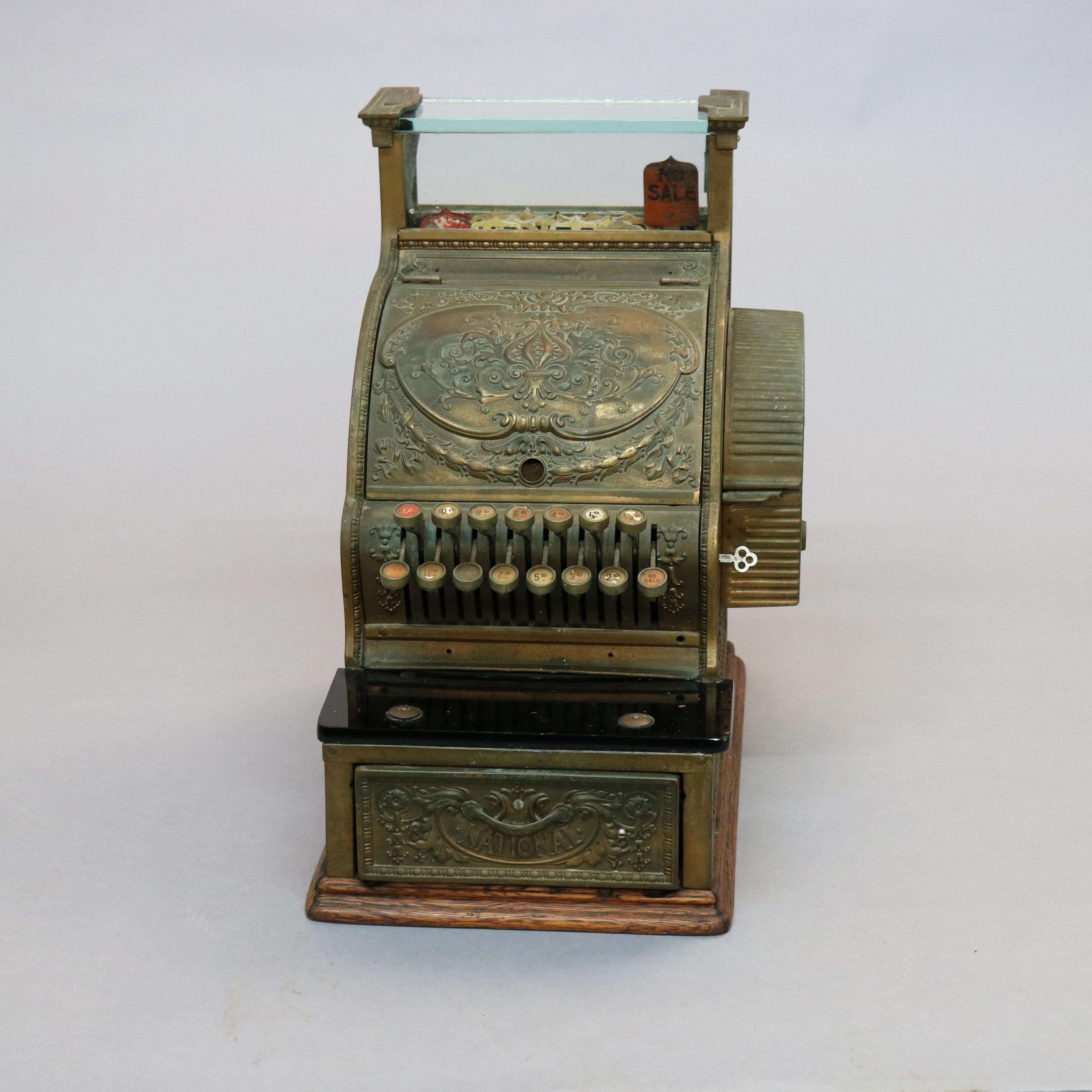 An antique country store cash register by National offers cast foliate and floral swag brass case having glass display, marble counter and seated on oak base, working and with key, c1900 

Measures: 17.25
