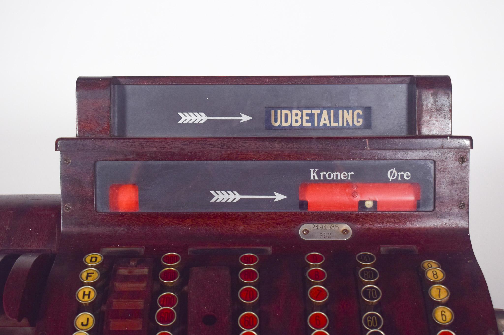 National cash register. Designed for transactions in Danish kroner (Kroner Øre). Constructed primarily of wood with metal buttons and crank.
The machine has several columns of numbered buttons, arranged to facilitate the entry of amounts