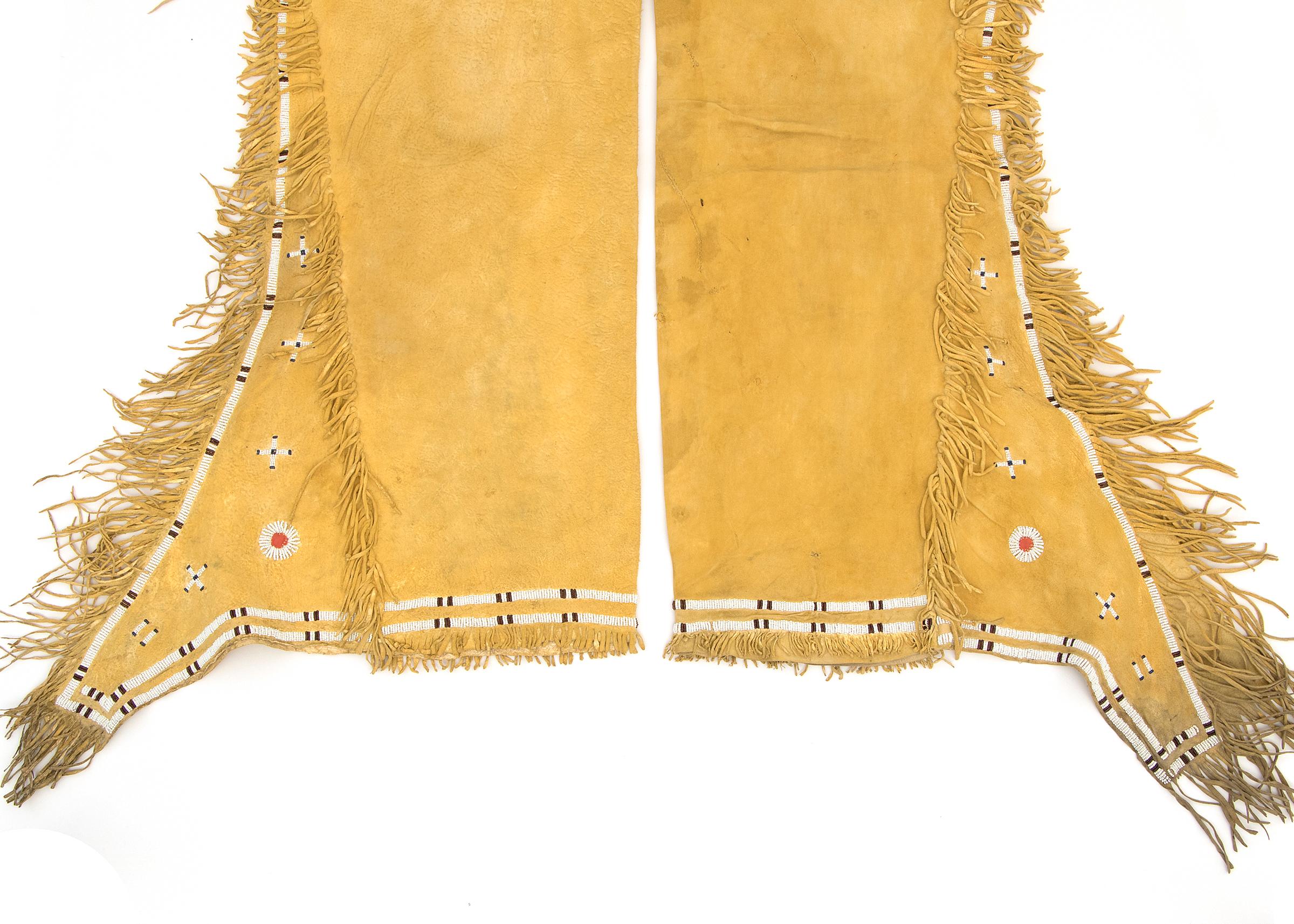 A pair of antique Native American Plains Indian beaded leggings constructed of native tanned hide and fringed. Partially beaded in black, blue and white trade beads with red trade cloth roundels. Dimensions listed are as shown for the pair, each