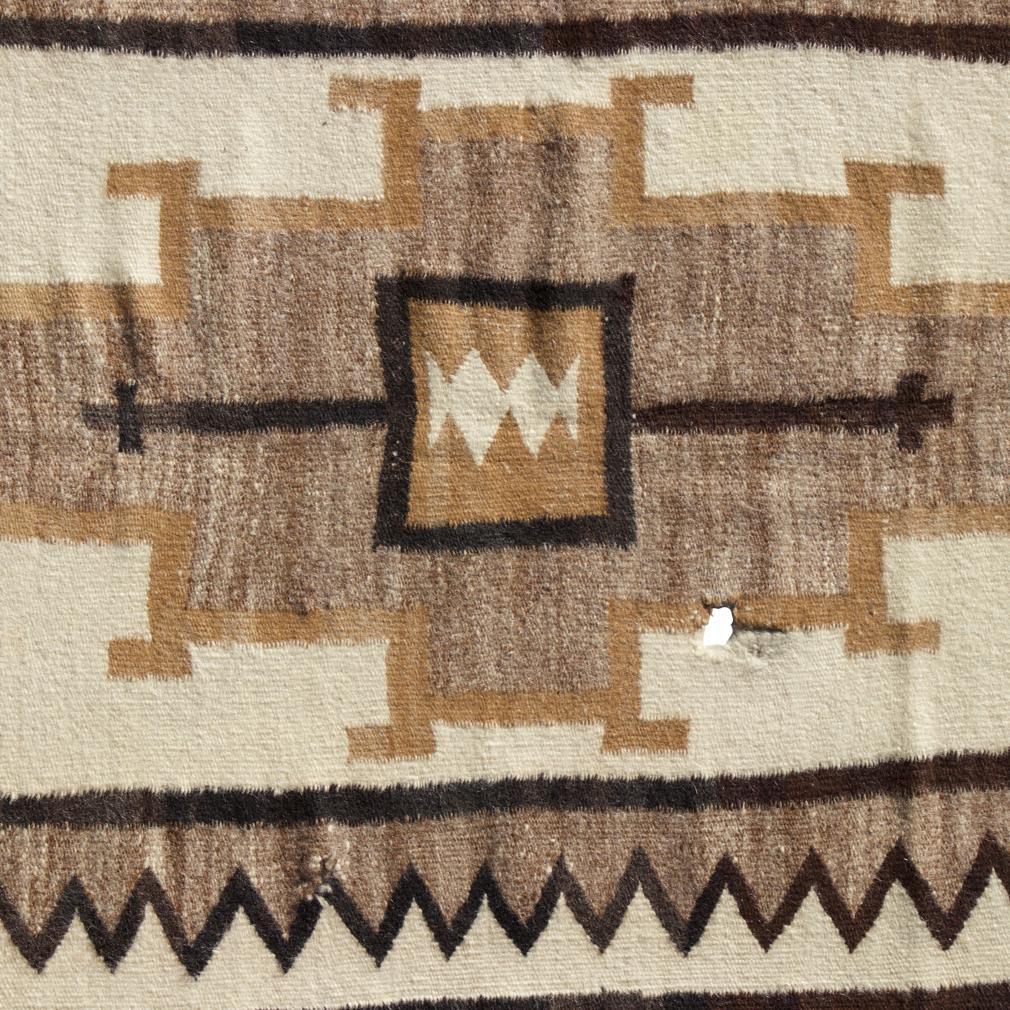 An antique Native Indian Navajo saddle blanket, Western United States. A natural dyed soft wool flat weave, wherein the design is the same on both sides. A white field with centre grey stepped design with beige outline and dark brown square with