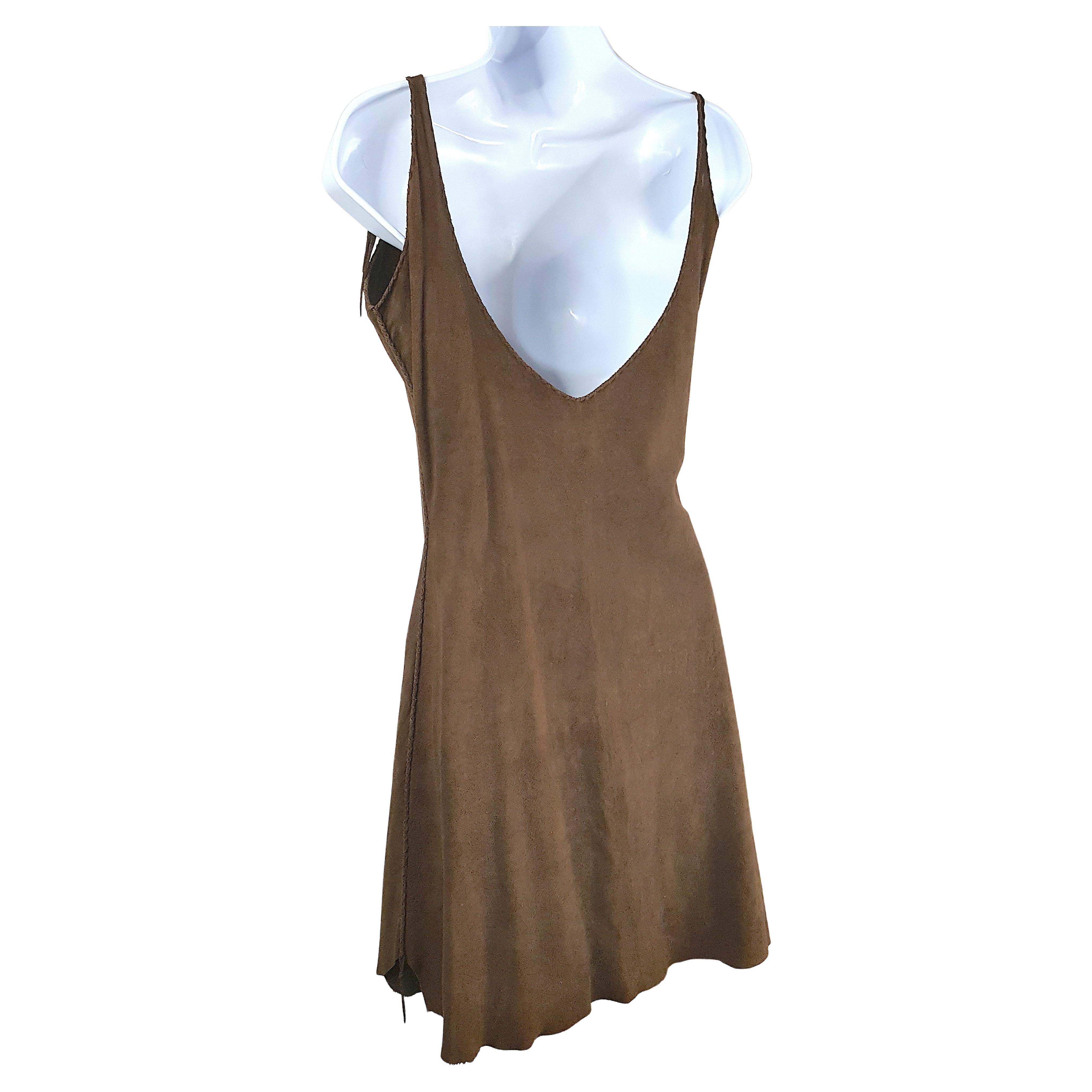 Cette ancienne robe chemise sans manches en cuir chamoisé brun, fabriquée à la main à l'époque des réserves, entre 1870 et 1930, est faite de deux peaux d'animaux souples et douces, ce qui donne une longueur d'ourlet légèrement irrégulière. Au lieu