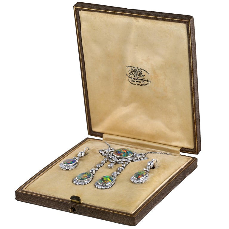 Presenting an extraordinary masterpiece of fine jewelry and history: A platinum natural Black Opal drop necklace and earring set. This exceptional piece showcases five oval-shaped cabochon cut black opals of impeccable quality, each bearing a