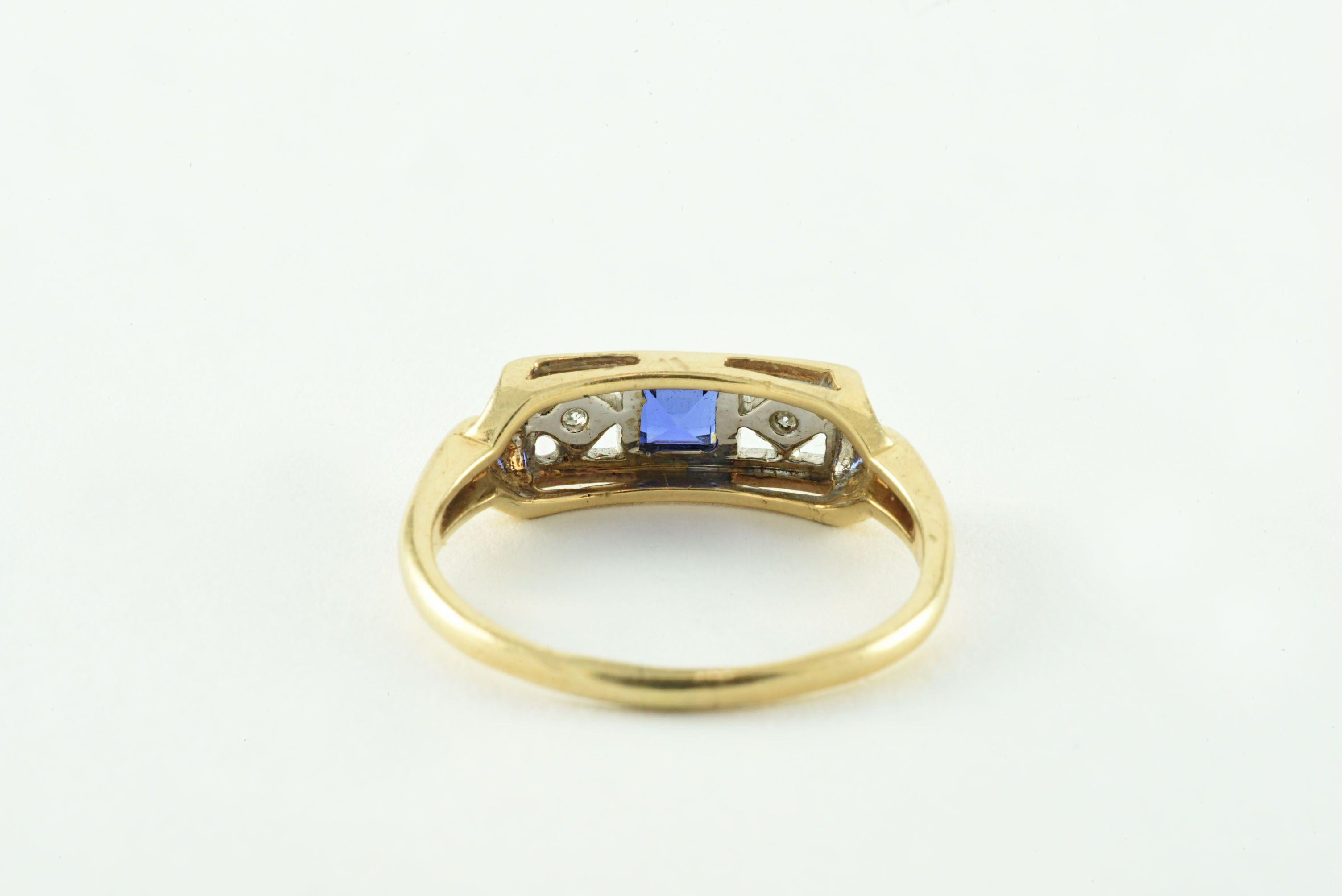 Crafted in the 1920s, this antique ring features a natural blue square-shaped sapphire accented east and west with two single cut diamonds totaling 0.02 carats in an openwork diamond design with delicate milgraining and framed in 14kt white gold