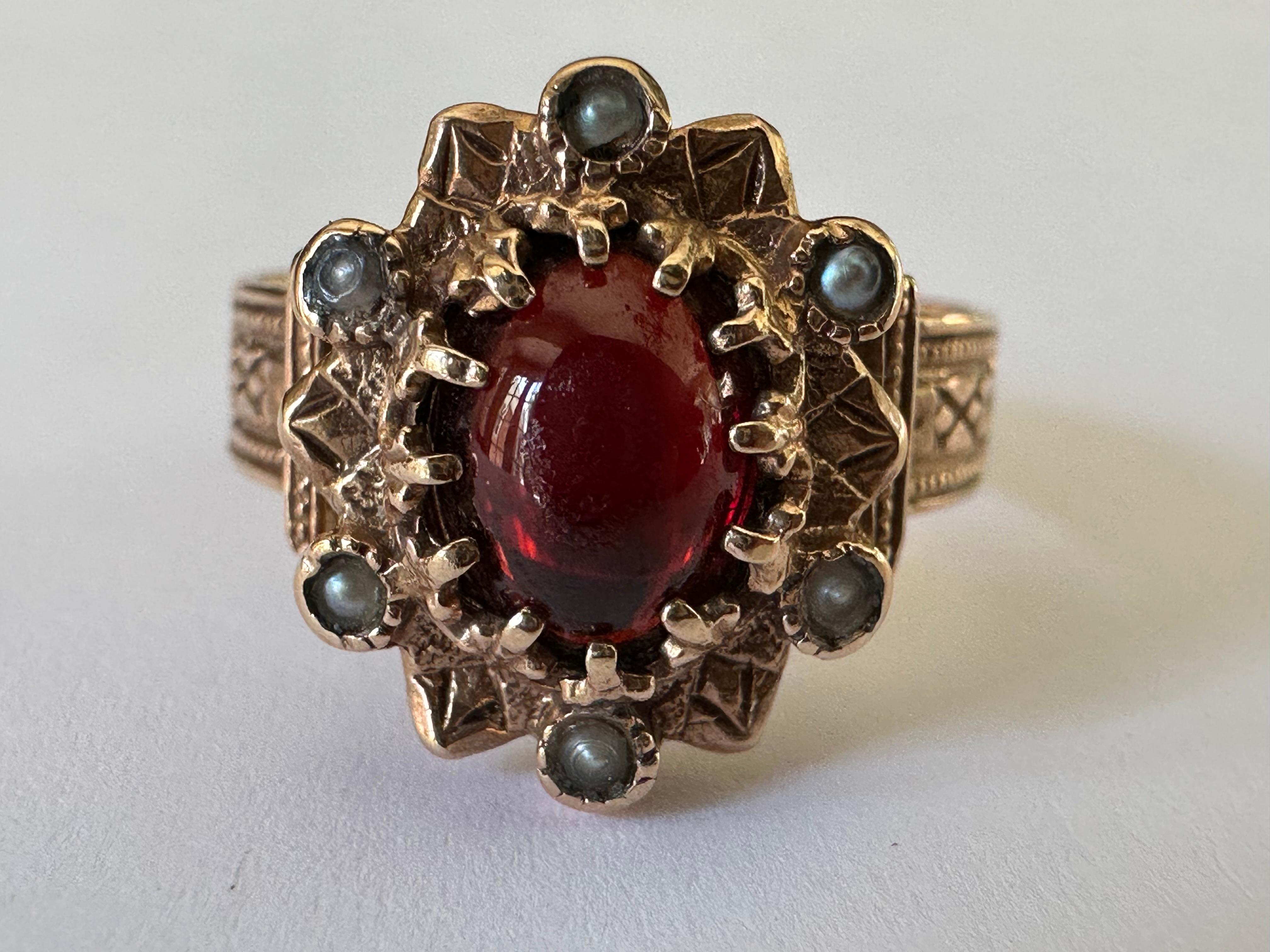 This beautiful antique Victorian ring features a natural oval-shaped cabochon garnet accented by six seed pearls set in an ornate band with fine hand engraving fashioned from 14K yellow gold. The markings on the band indicate the ring was most