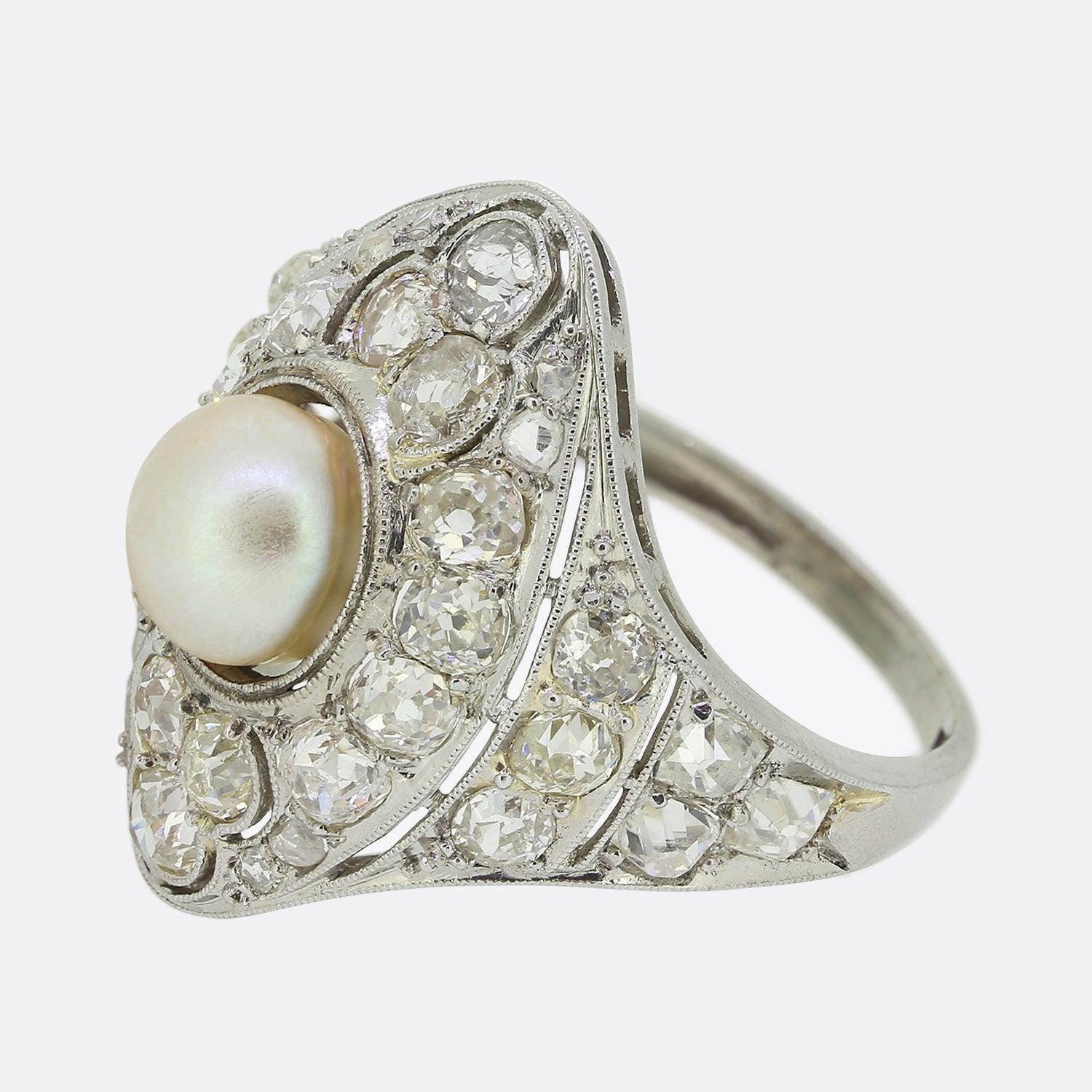 Ecco uno splendido anello a grappolo con perle e diamanti risalente ai primi anni del XX secolo. Una perla naturale rotonda con un bel livello di lucentezza si trova al centro del quadrante, con un ampio sfondo di diamanti tondi sfaccettati di