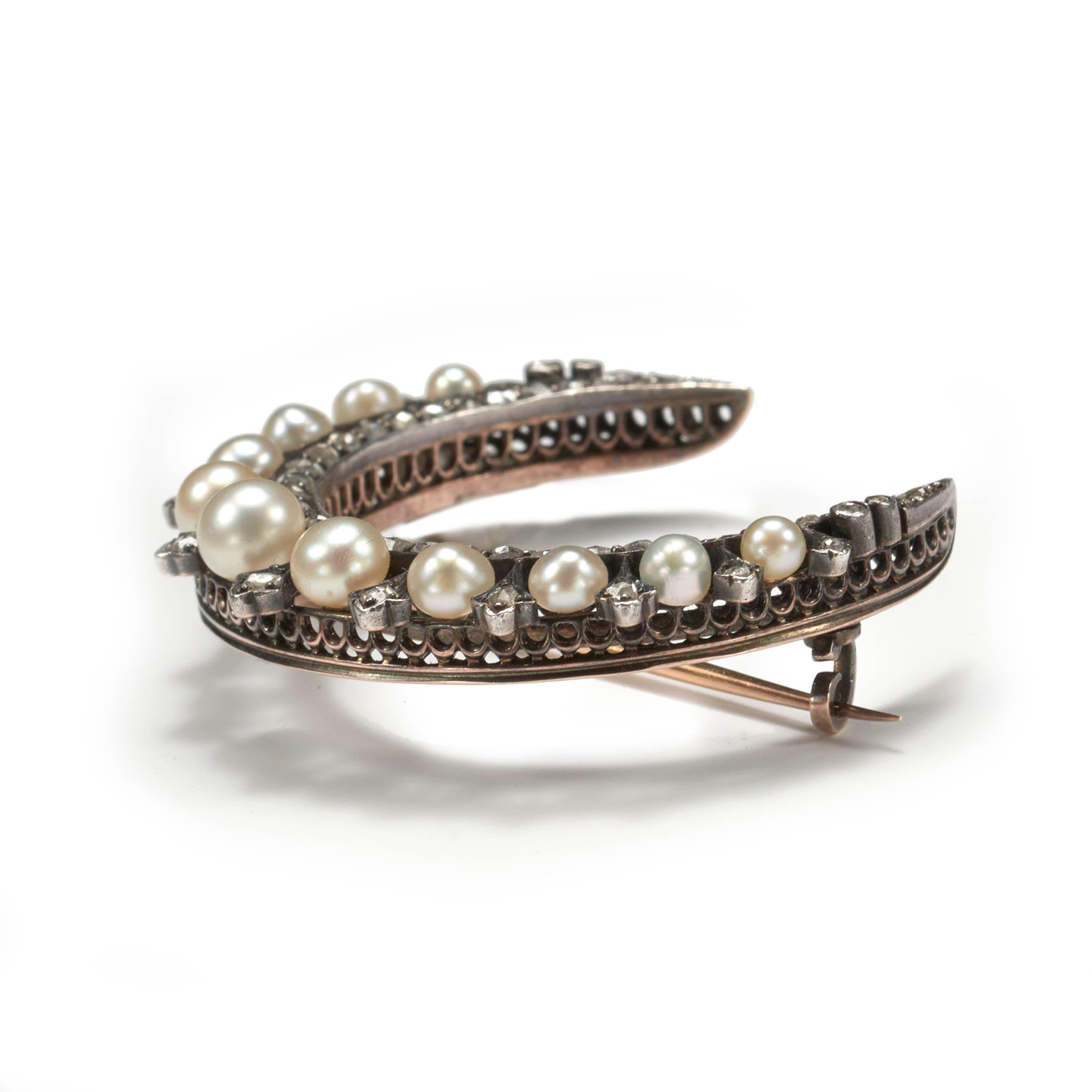 An antique crescent brooch, set with natural pearls, graduating from the centre, spaced with tapered settings with rose-cut diamonds, and an inner row, grain set with rose-cut diamonds, mounted in silver-upon-gold, on a gold pierced gallery, circa