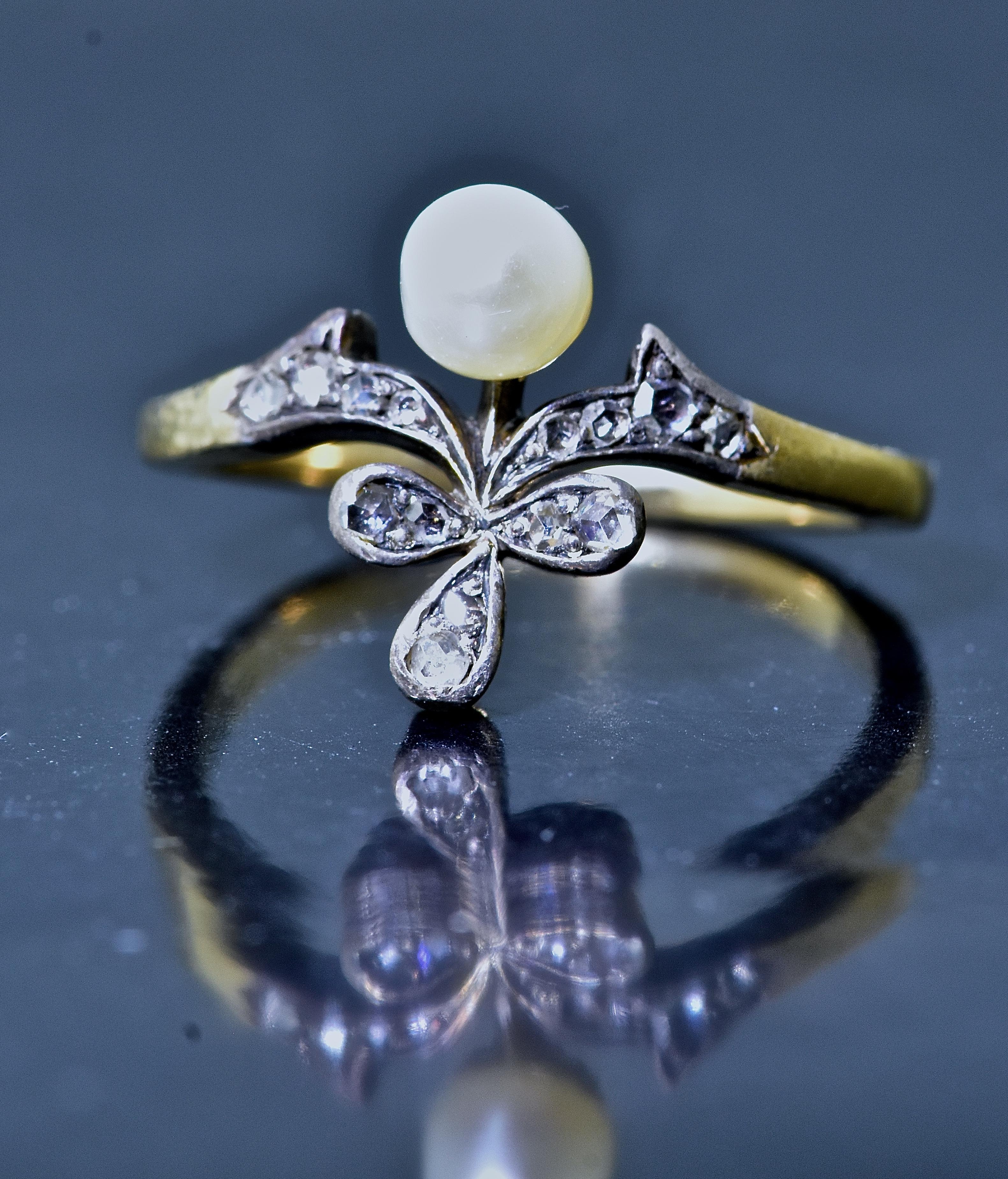 Antiker Ring aus 18K und Silber mit natürlicher Perle.  Die Perle misst 4,83 mm und ist naturbelassen,  im Gegensatz zu gezüchteten und sehr leicht unrunden.   Das Blumenmotiv ist mit 14 perlenbesetzten Diamanten im Rosenschliff (ungefähres