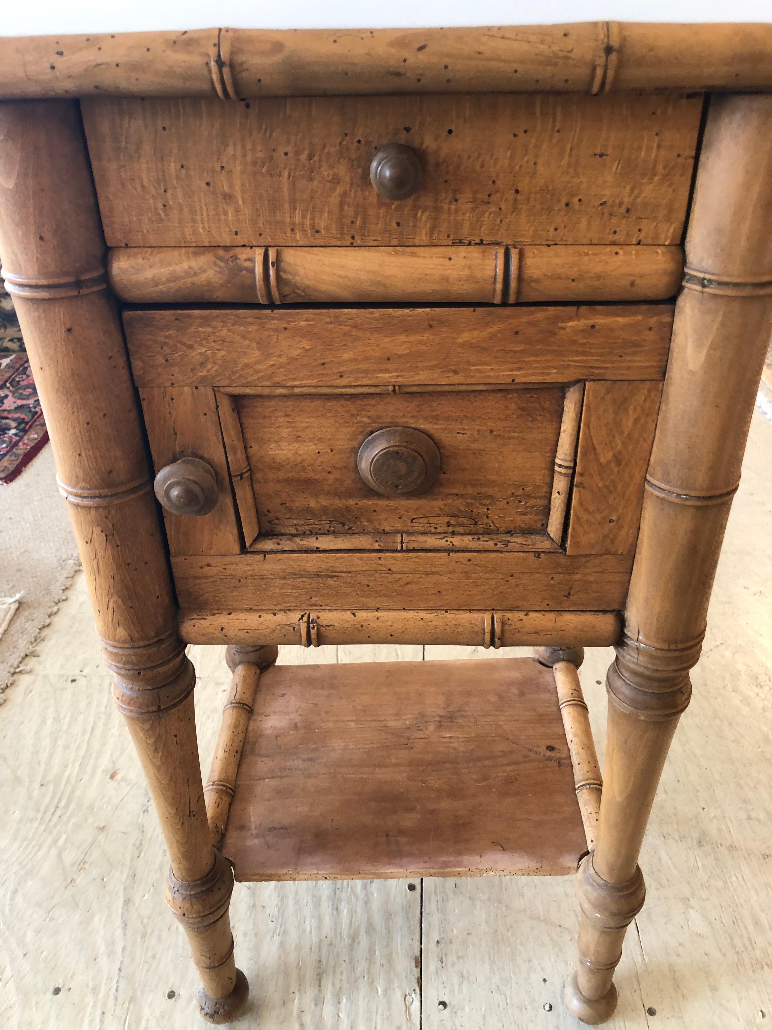 Charming unfinished antique natural pine night stand or end table having single drawer over paneled door with storage inside.  The frame of the stand has the look of bamboo.  The white marble top is not original.