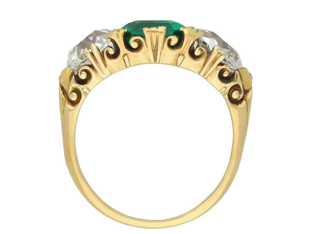 Victorian Colombian emerald and diamond carved three stone ring. Set to centre with an octagonal step-cut Colombian Muzo emerald with no colour enhancement and insignificant clarity enhancement in an open back triple claw setting with an approximate