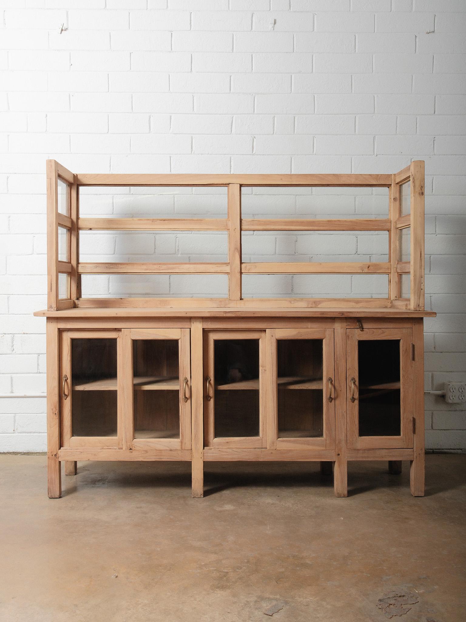 Un sorprendente bancone in legno naturale anticato con conigliera superiore, realizzato con superfici splendidamente invecchiate e pannelli in vetro trasparente che offrono una visibilità aperta pur mantenendo il suo carattere artigianale e senza