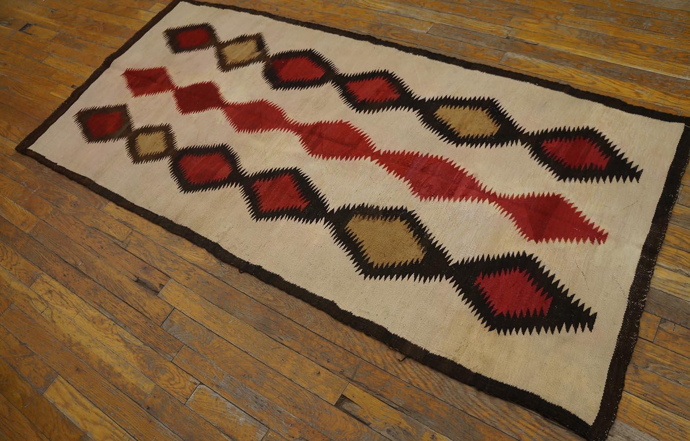 Ce petit tapis long amérindien tissé de manière farfelue présente un champ écru décoré de trois colonnes indépendantes et flottantes, chacune composée de six losanges dentelés au charme erratique, dans des tons anthracite, camel clair et rouge
