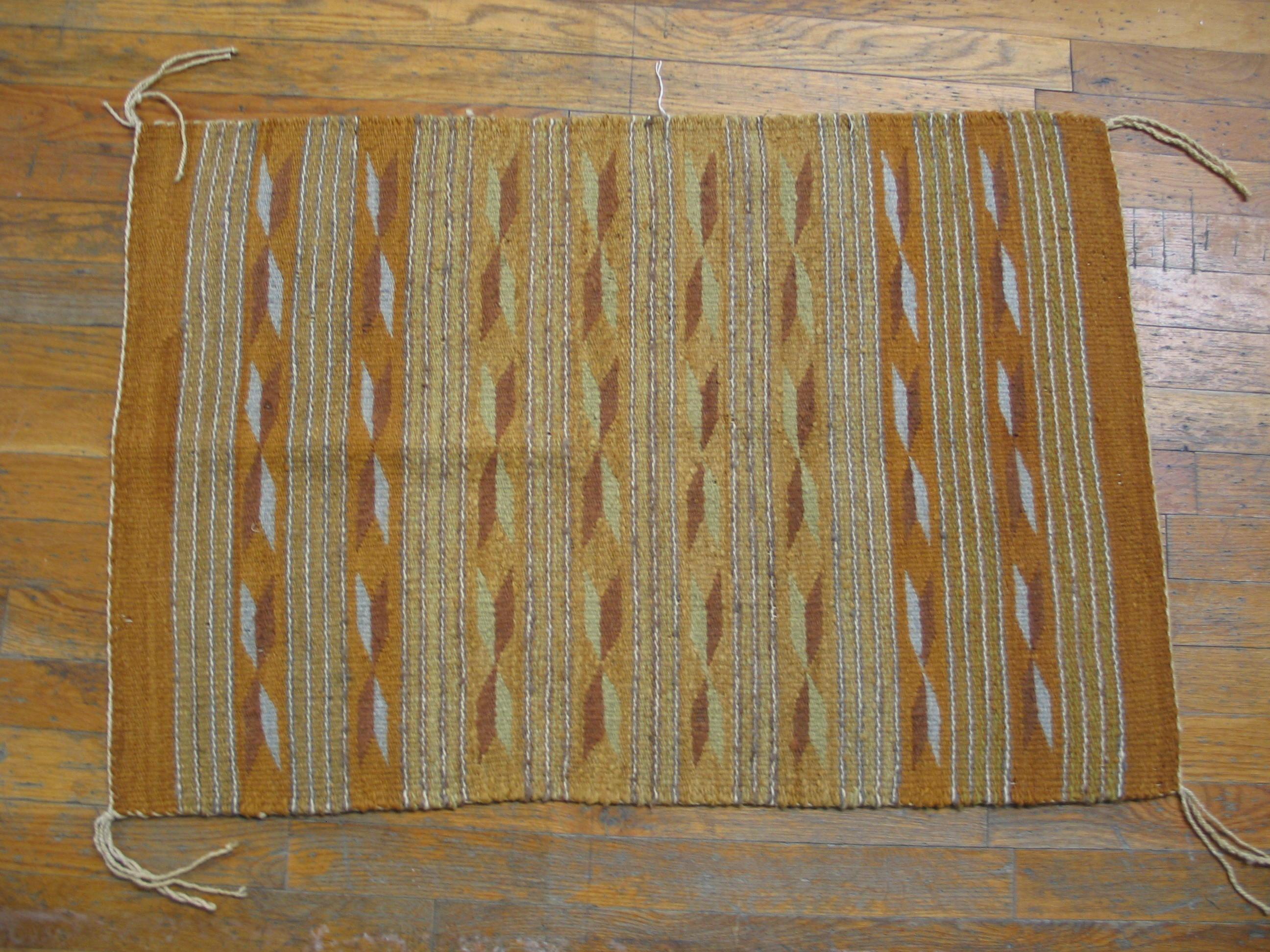 This Chinle-style mini-blanket / ruglet shows an eight band pattern of rust and straw and ivory feathery bows with quadruple lines separating them. Makes a good pillow. Good condition. 