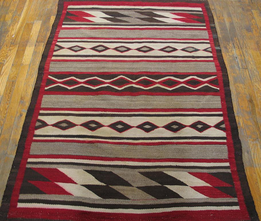 This is a Chinle-style rug with the characteristic horizontal banded pattern, measures: 4' 0” x 5' 5”. Here the light grey bands alternate with wider patterned sections with tilted lozenges in red, black ecru and grey; chained small lozenges on