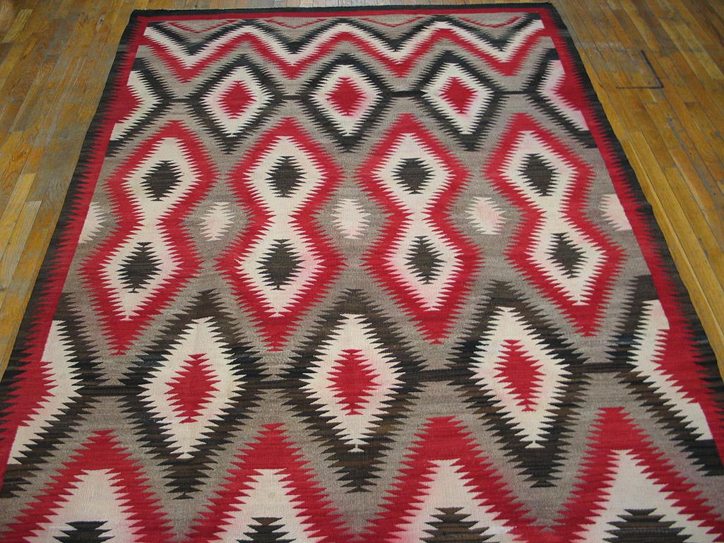 This rare small carpet format Navajo piece has a light grey natural wool field covered by serrated and similarly drawn, nested lozenges and chevroned triangles, detailed in red., black and ecru. The central red pinched double lozenges are flanked by