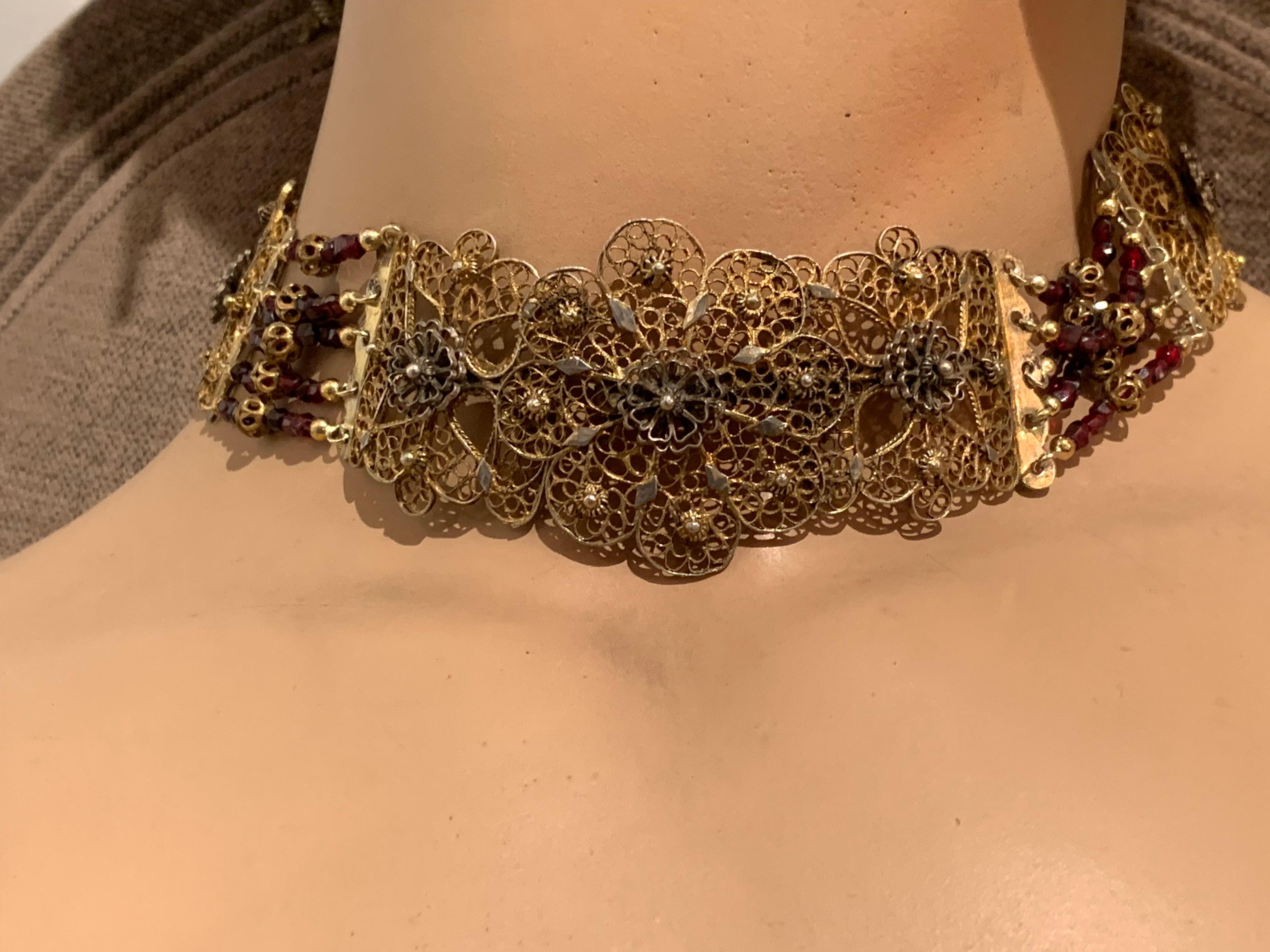 Late 18th century garnet and silver filigree choker that fastens at the front with an ornamental clasp.  Six pierced panels with cut out flower motive are connected by five rows of facetted garnet beads. Each row of beads fearures a bead, made out