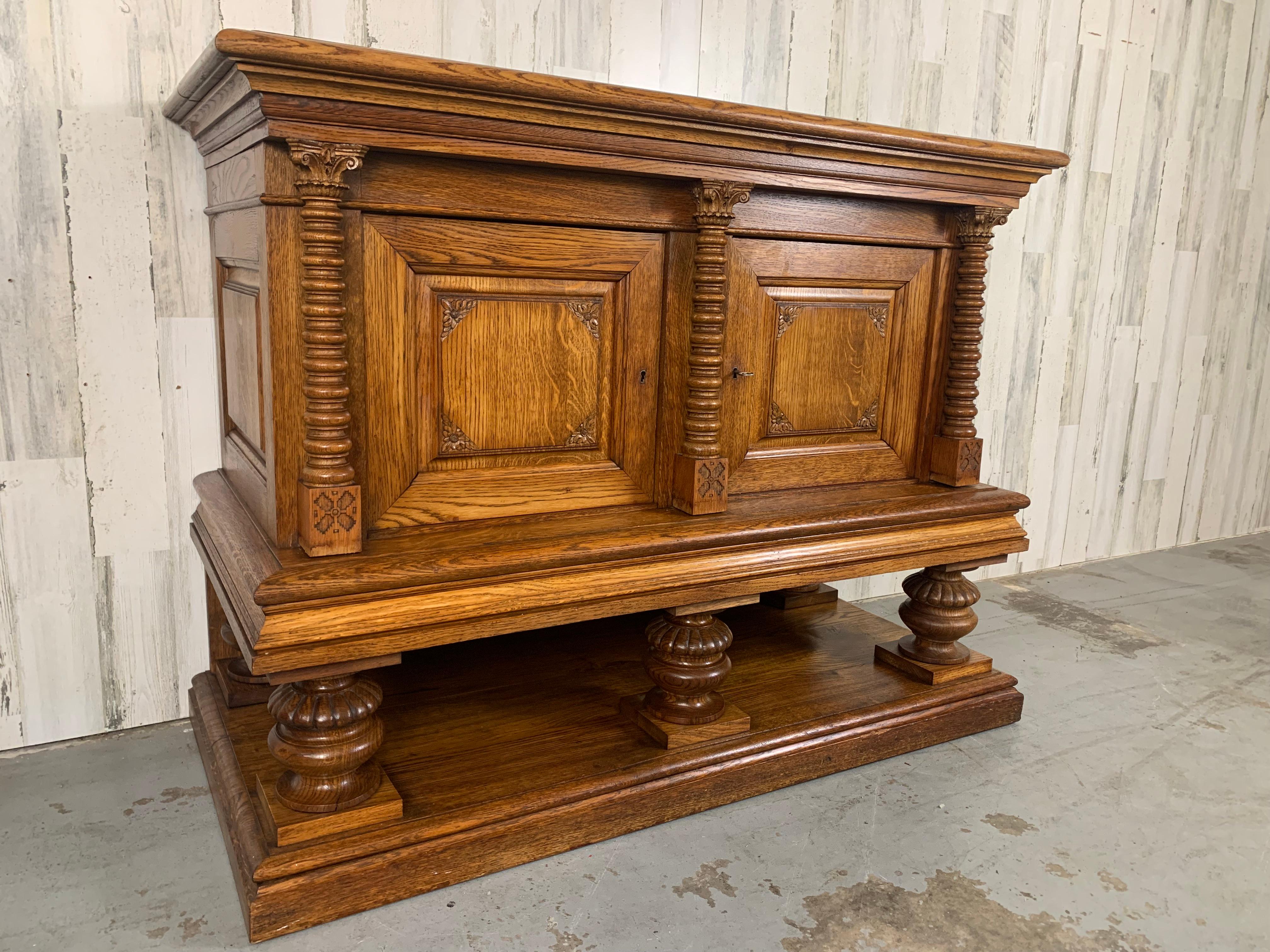 Very solid little cabinet with corinthian topped columns and massive carved legs on top of a platform. The doors and sides are deep paneled for that sturdy look. There is one working key.