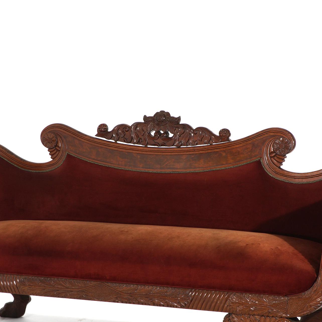 ***Ask About Reduced In-House Delivery Rates - Reliable Professional Service & Fully Insured***
An antique American Empire Greco upholstered sofa offers walnut and burl construction having floral carved crest, scroll arms, foliate elements and paw