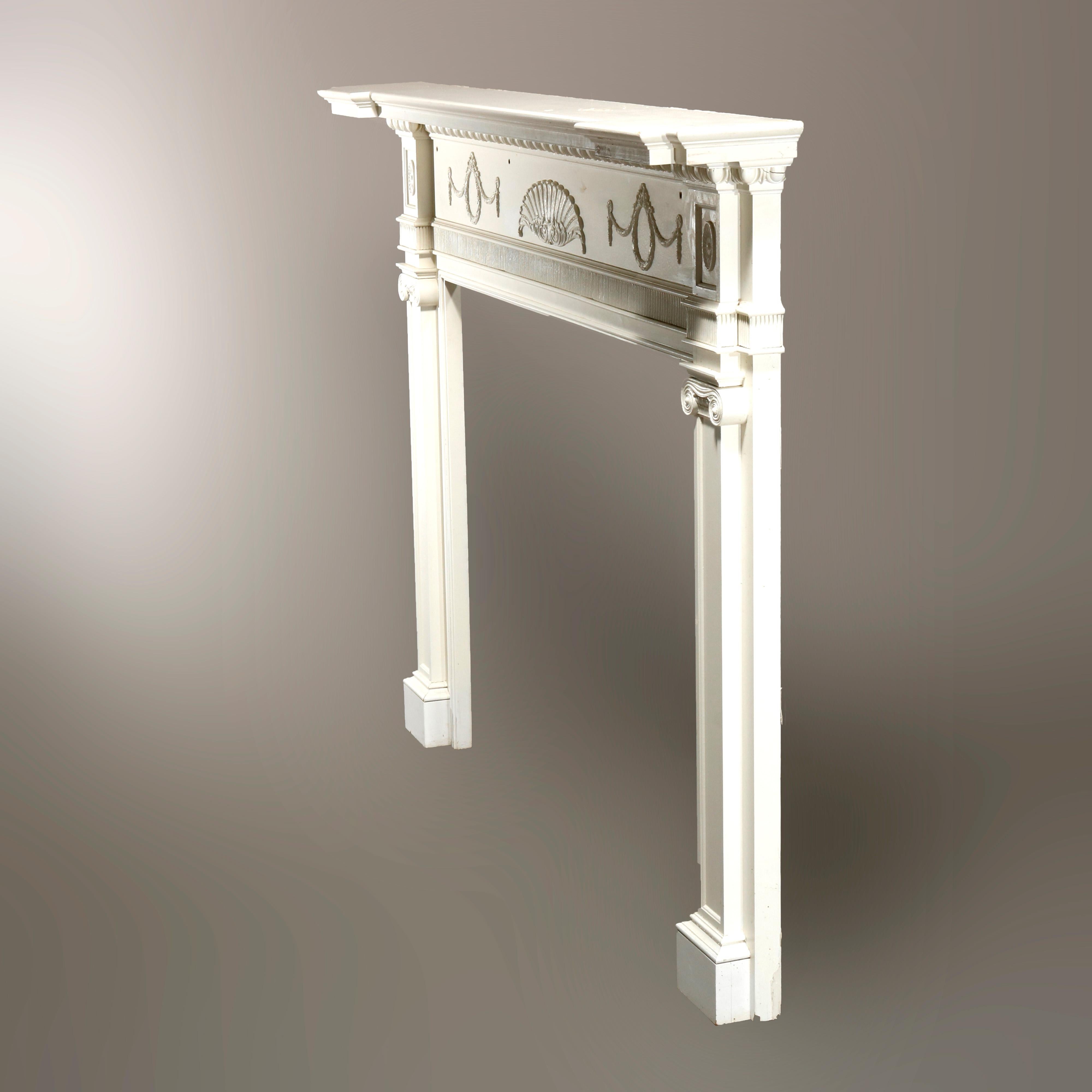 An antique neoclassical architectural fireplace mantle offers wood construction with frieze having applied repeating wreath and swag garland elements, carved egg-and-dart and reeded trim, with flanking Corinthian column supports, painted white, 20th