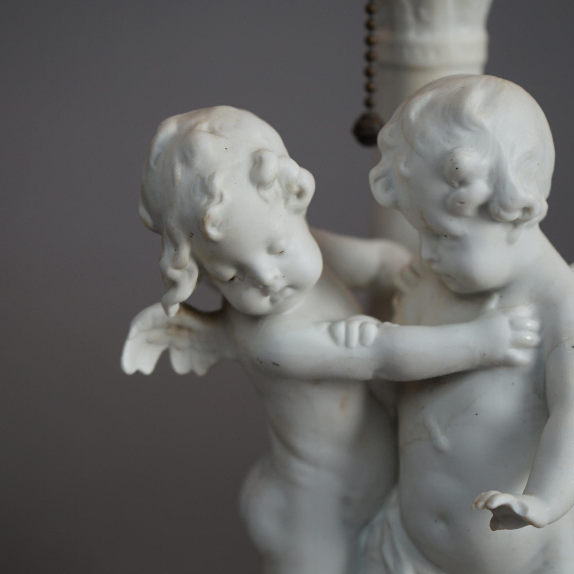 An antique Neoclassical figural table lamp offers slag glass panel shade over parian porcelain double socket base with cherubs, c1920

Measures - 20.5