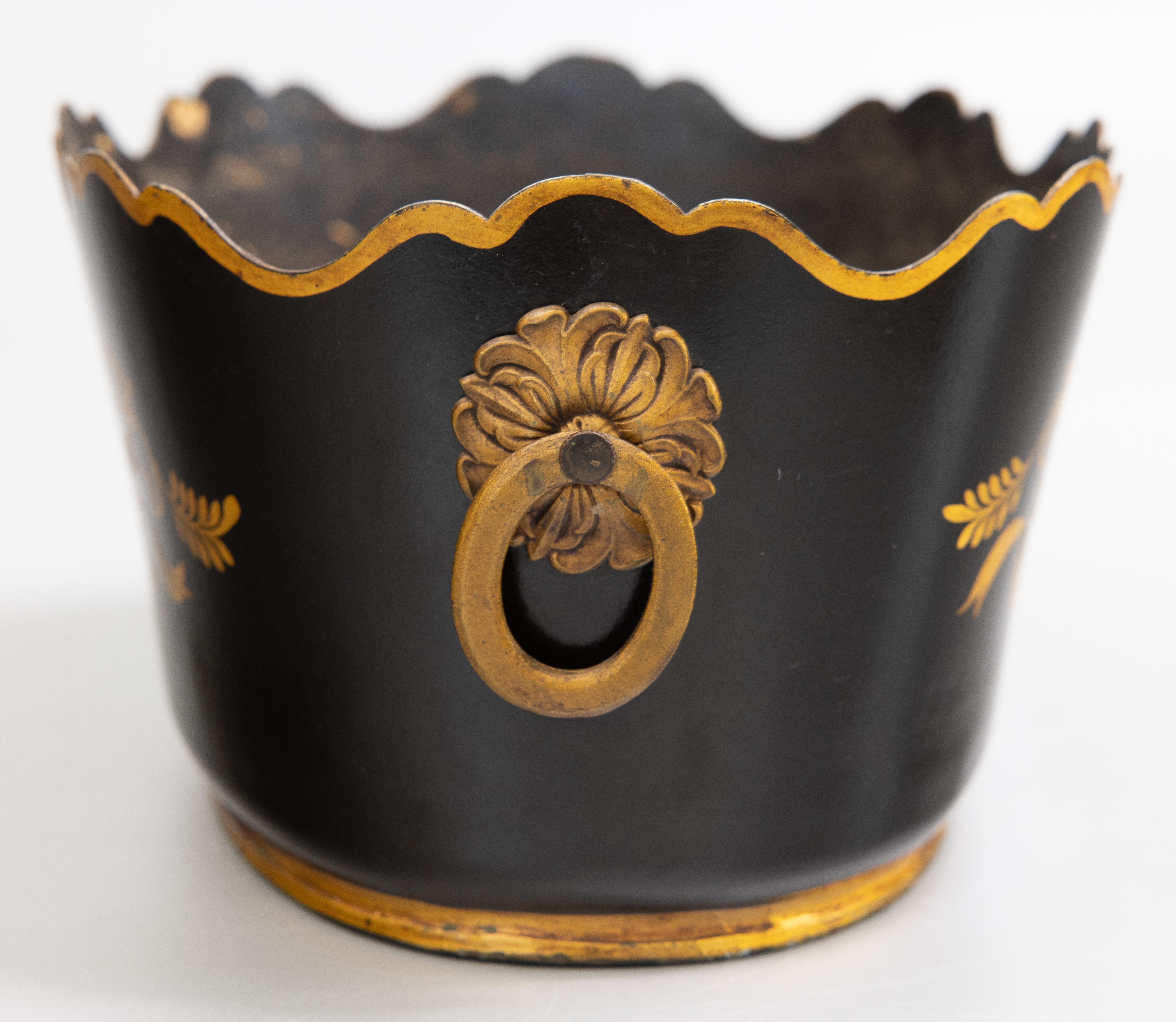 A lovely antique early 20th century French black and gold toleware monteith cachepot. This gorgeous jardiniere has hand painted gilt arrows, scrolling leaves and ribbons with lovely ring handles and a beautiful scalloped rim. It's perfect for