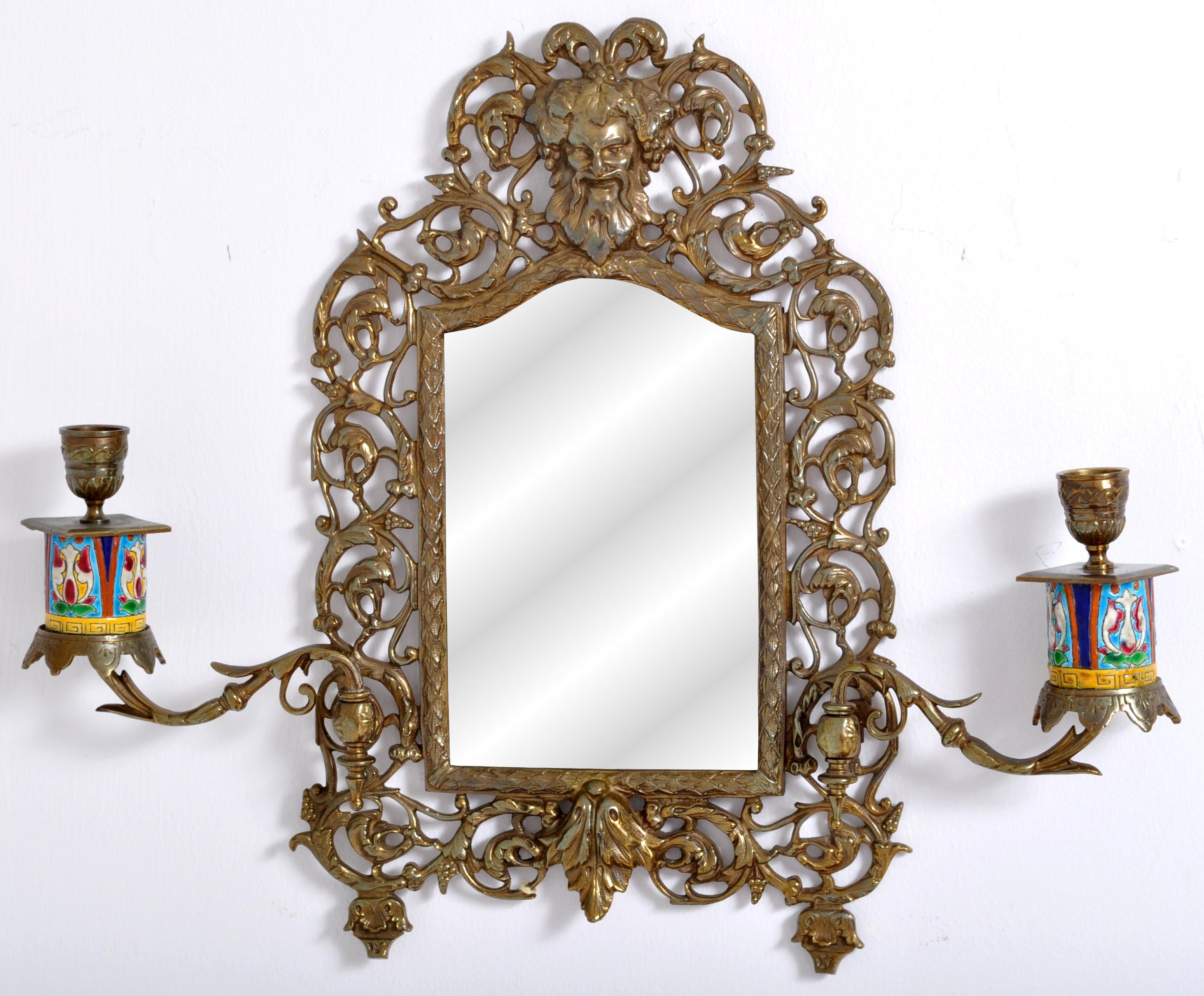Antique neoclassical French brass wall mirror with candle sconces, circa 1890. The mirror having a pierced floral brass frame and mounted with a mask of the Roman God Bacchus, the frame enclosing a beveled arched mirror. The mirror having a pair of