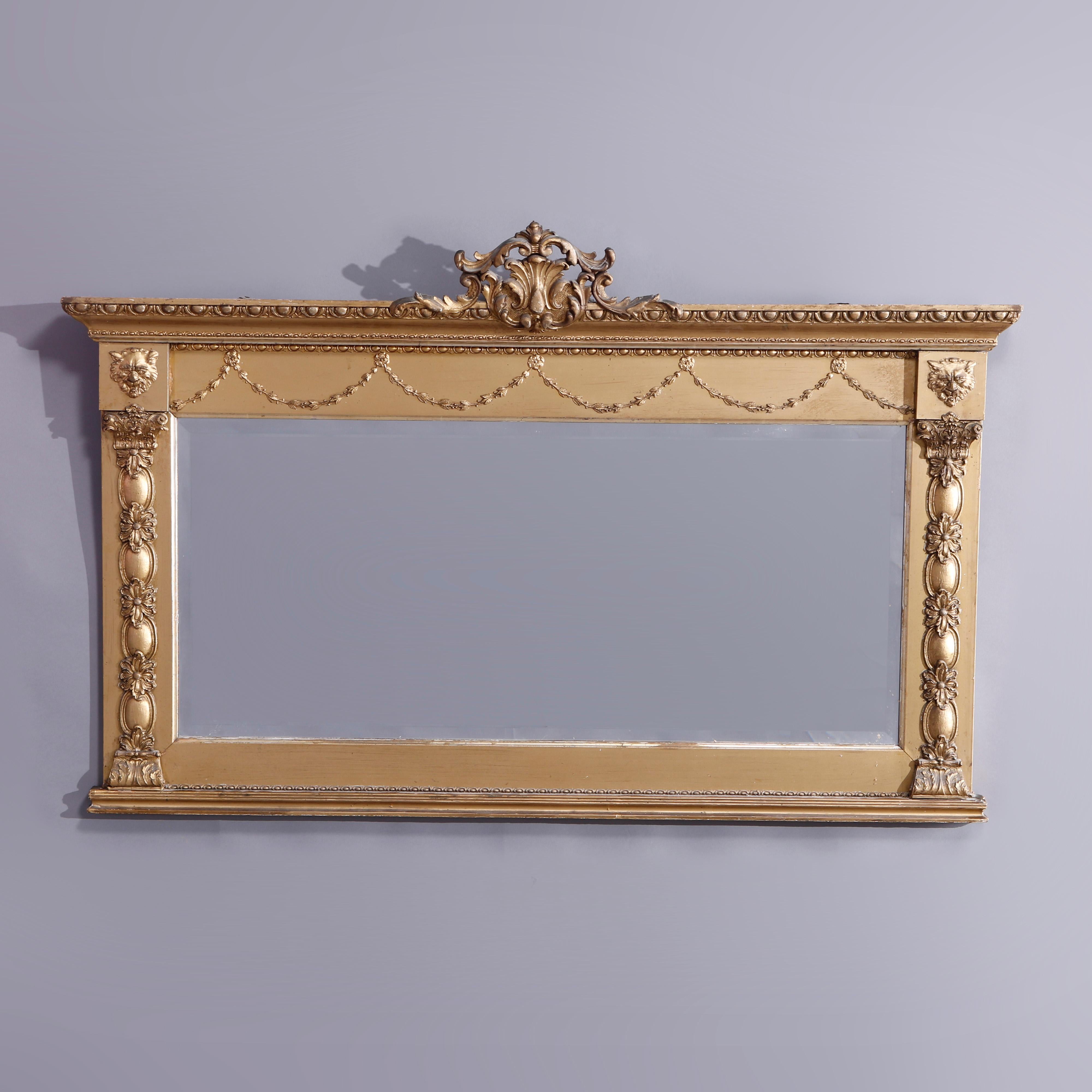 An antique large neoclassical wall mirror offers giltwood construction in horizontal form with scroll and foliate pierced crest over frieze with drape garland elements and lion rosettes surmounting mirror with flanking stylized Corinthian column