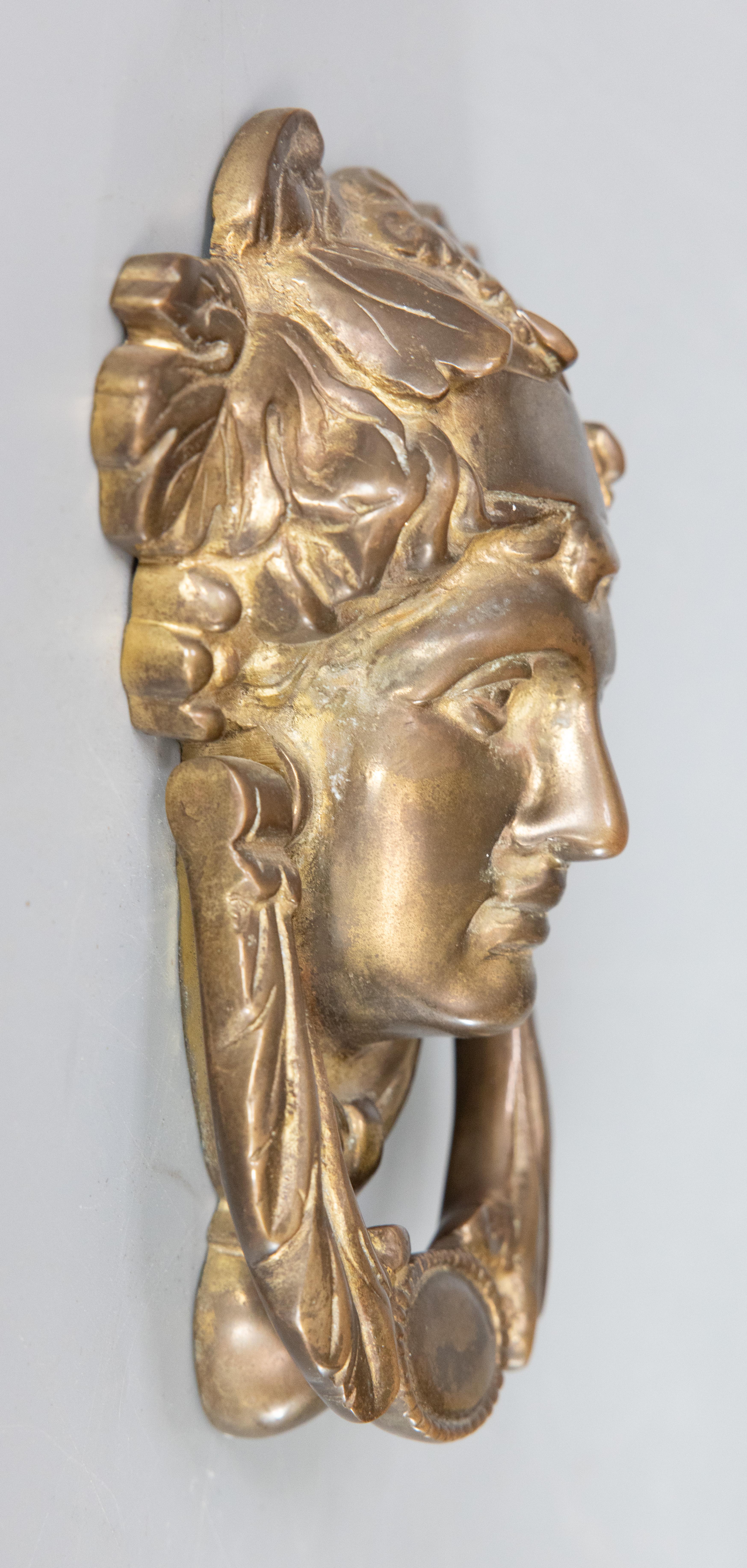 A superb antique early 20th-Century English brass door knocker in the image of the Greek goddess Athena. This fine door knocker is solid and heavy, weighing approximately 3 lbs, surrounded by scrolling foliage in a lovely patina. It would be a
