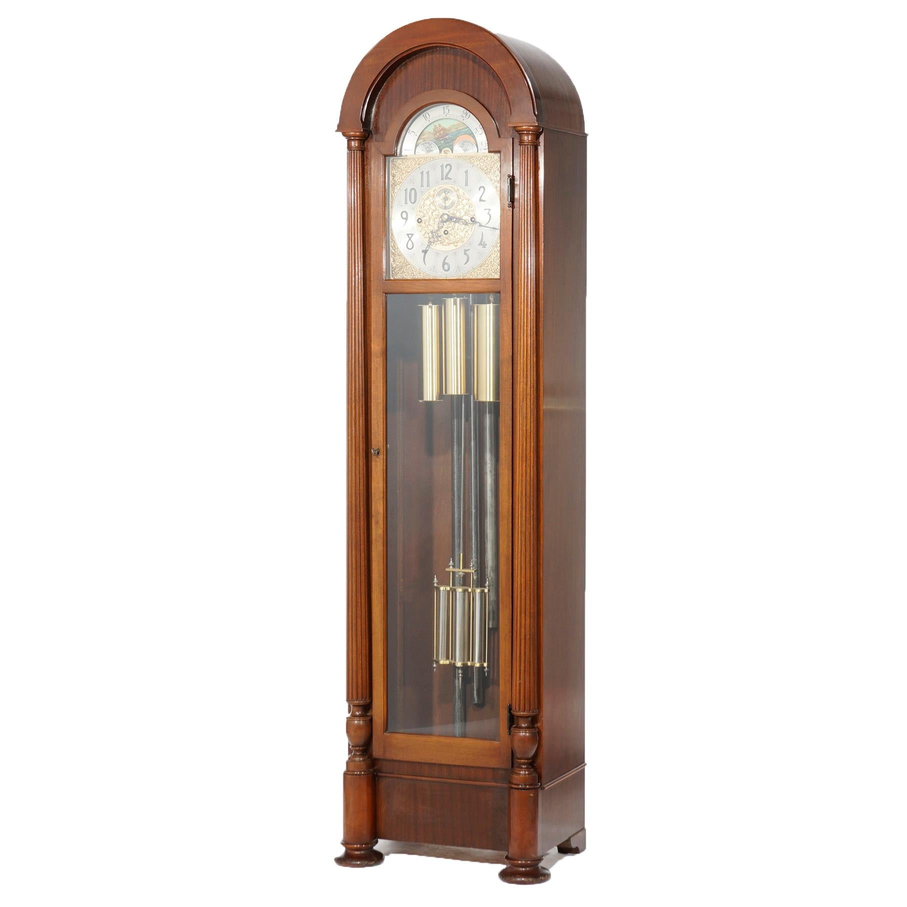 An antique tall case clock by Herschede offers mahogany case in arched form with central glass door and flanking columns, 