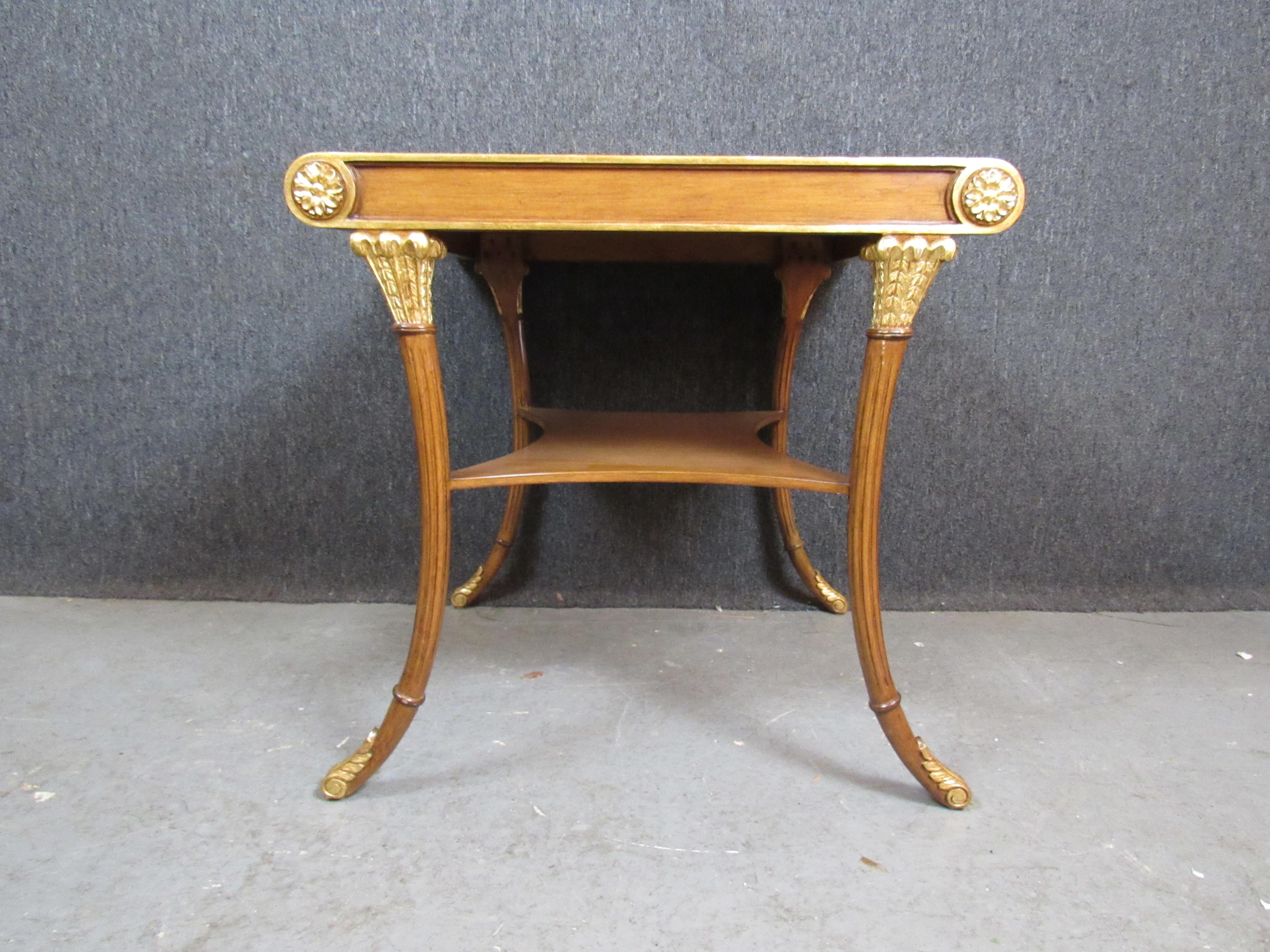 Elevate any space with a sense of history and luxury with this exquisite Neo-Classical Revival mahogany table. Beautifully curved legs are adorned with gilded, feathered feet while a deeply curved lower tier offers storage or display space. A