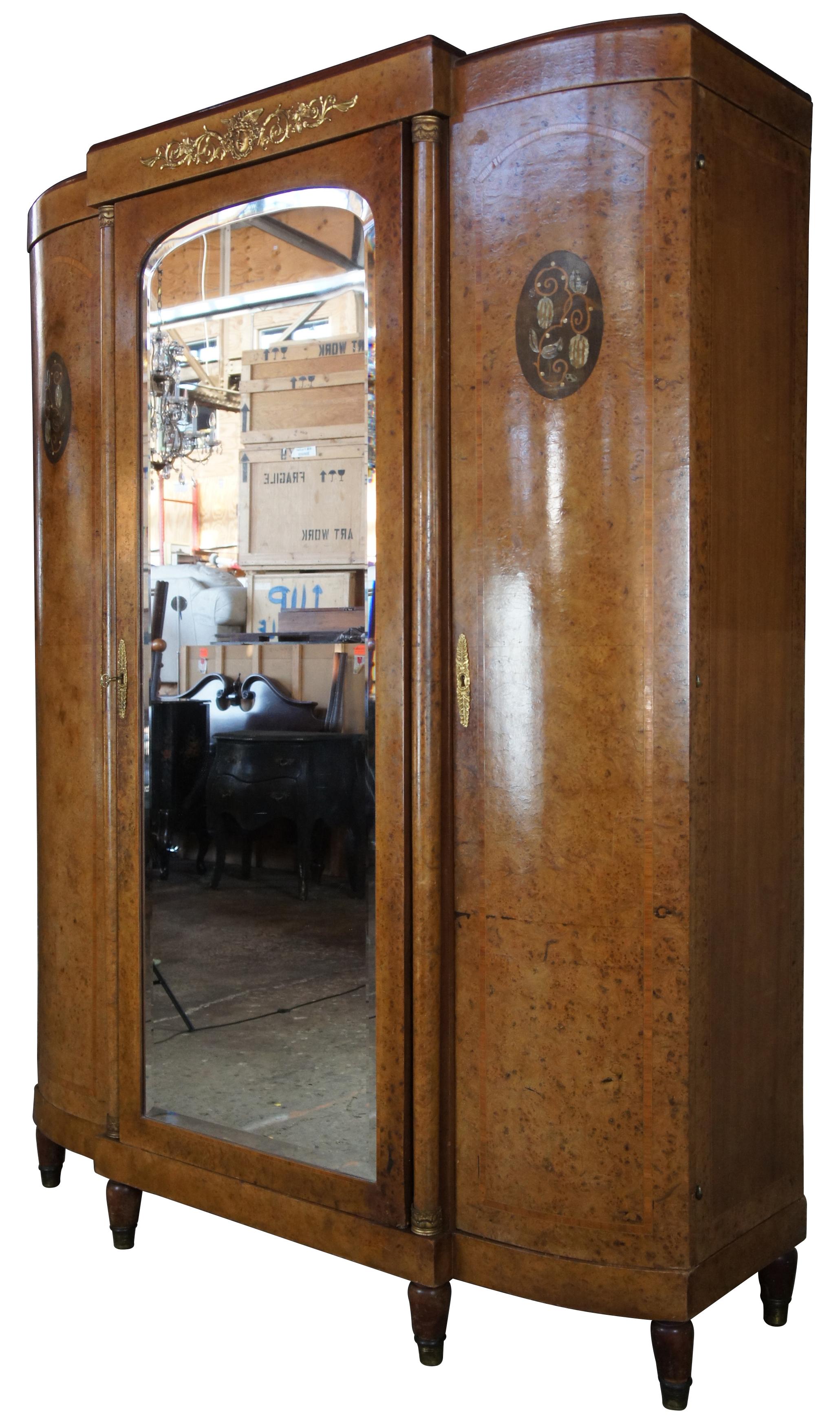 Neoclassical knockdown armoire. Made from walnut and olive burl veneer with marquetry inlay and mother of pearl along doors. Features a large central beveled glass mirror flanked by columns and gilt bronze mounts. The cabinet is supported by tapered