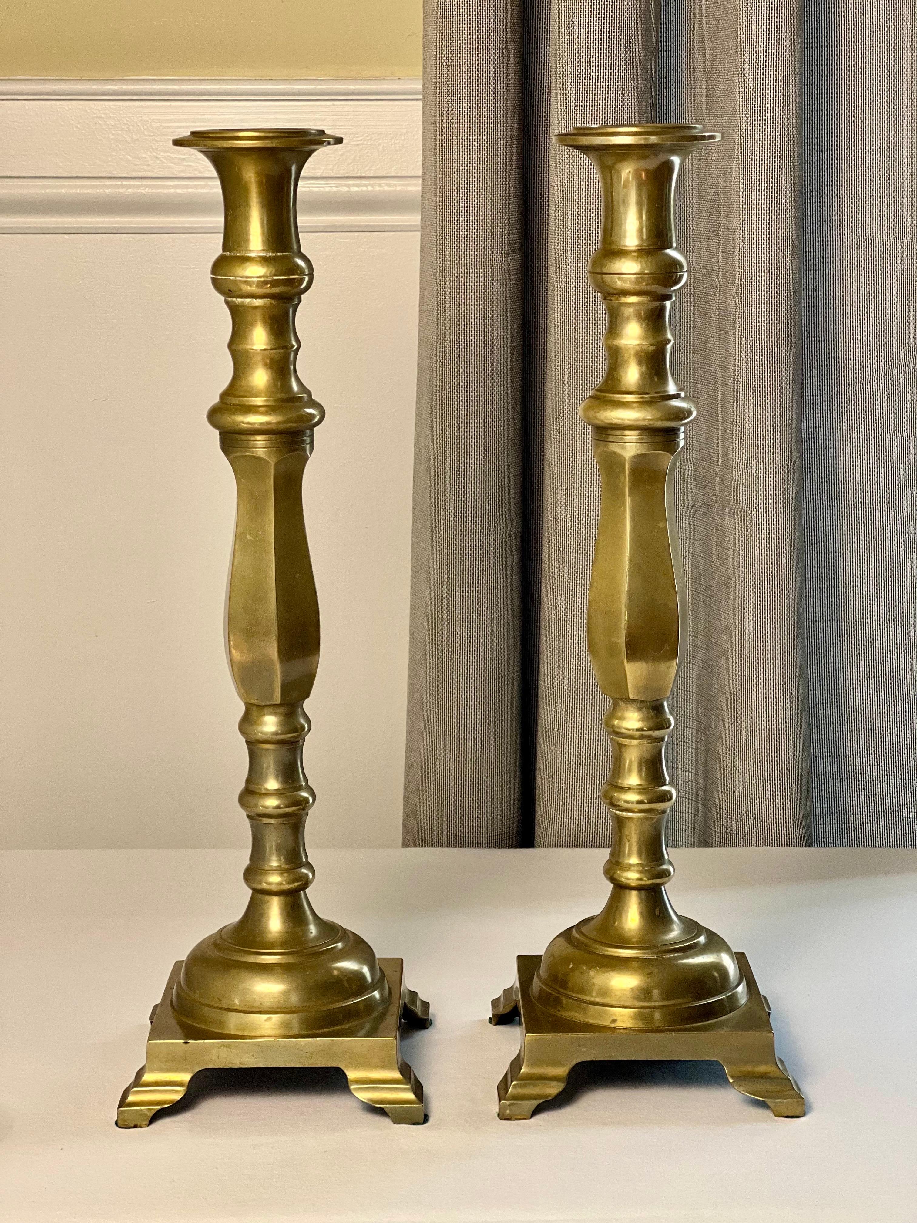 Coppia di candelabri neoclassici in ottone a forma di balaustro con base quadrata, metà o fine del XIX secolo.  Hanno un'altezza extra in una forma elegante e simmetrica, con un gambo tornito che poggia su una base unica a gradini con piedi ad