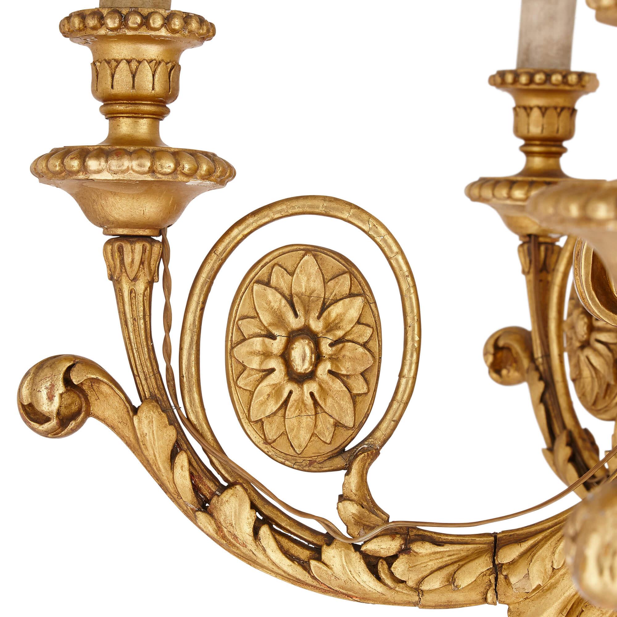 Lustre ancien en bois doré sculpté de style néoclassique
Français, 19ème siècle
Mesures : Hauteur 84 cm, diamètre 82 cm

Cet élégant lustre en bois doré sculpté est réalisé dans le style néoclassique. Le lustre présente un corps en bois doré de