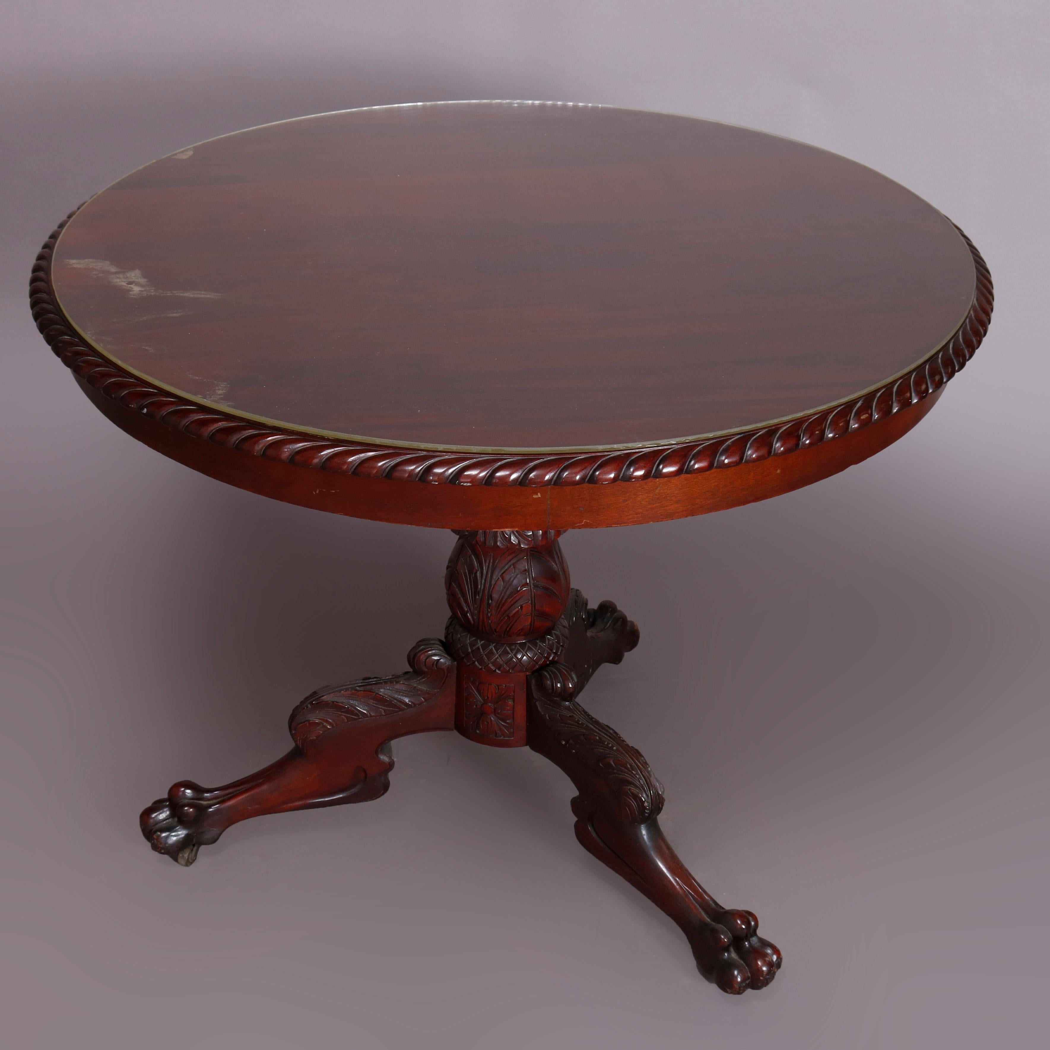 An antique neoclassical style center table offers mahogany construction with circular top having carved rope twist bordering and surmounts a foliate acanthus carved column raised on three legs having scrolled acanthus knees and terminating in paw
