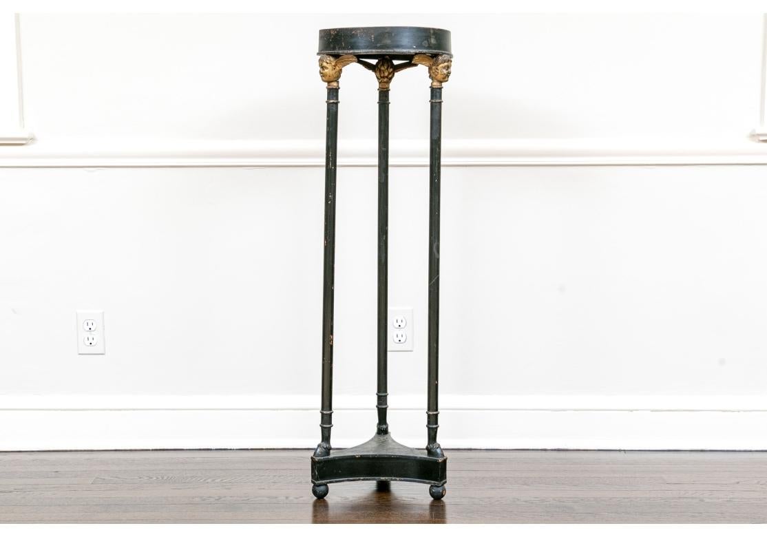 A stately Neoclassical style fern stand on three feet, with a trefoil form stretcher. Three cylindrical pillars rise upwards to the carved and gilt finished Neoclassical style mythological winged heads which support the circular table