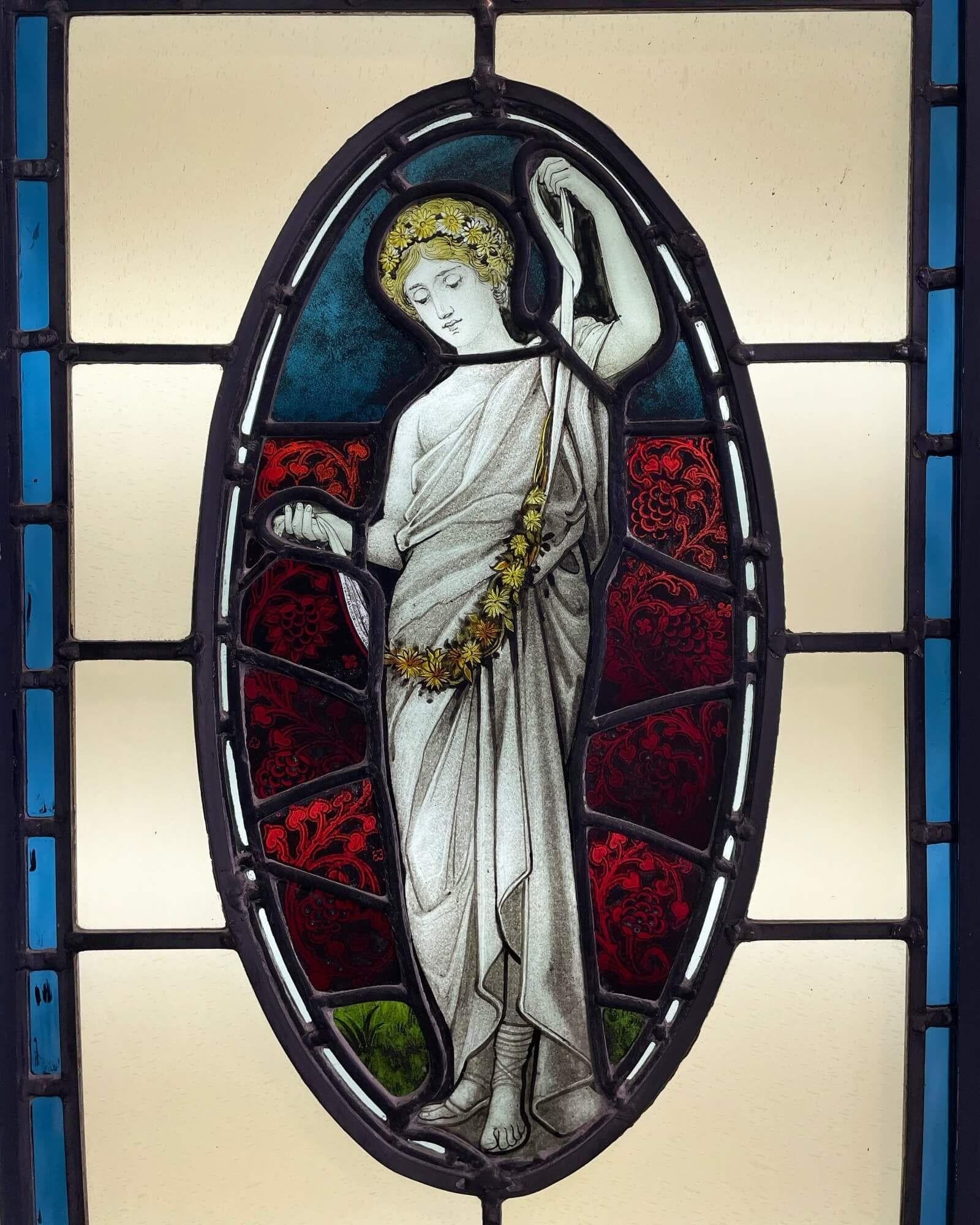 An elegant large neoclassical style stained glass window circa 1890. A Victorian take on a neoclassical design, this stained glass window centres around an elongated oval panel depicting a female dressed in white drapery, with flowers in her hair,