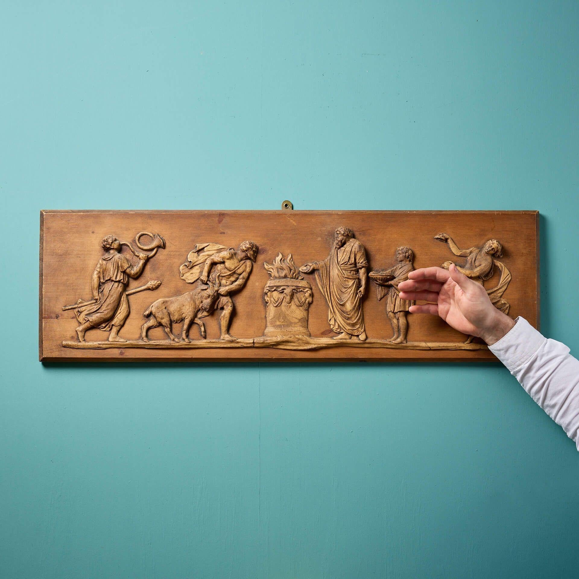 Panneau ancien de style néoclassique en pin et composition sculpté, datant du début du 20e siècle.
 
Sous la forme d'un grand paysage, ce panneau artisanal présente une scène néoclassique de personnages en tenue classique autour d'un foyer, certains