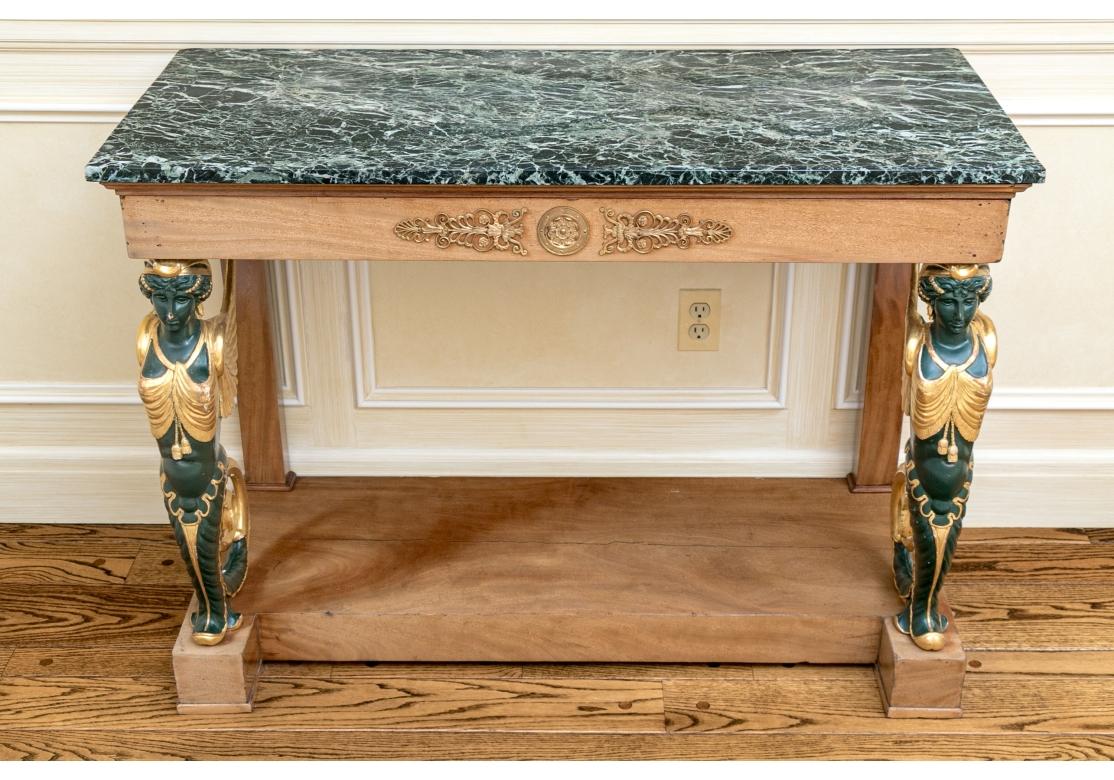 An exceptional Console with carved, painted and gilt Sphinx supports and veined green marble top. In an unexpected and fine lighter wood with gilt mounts on the apron front. The Winged Sphinx are strongly carved and wear tasseled gilt garments and