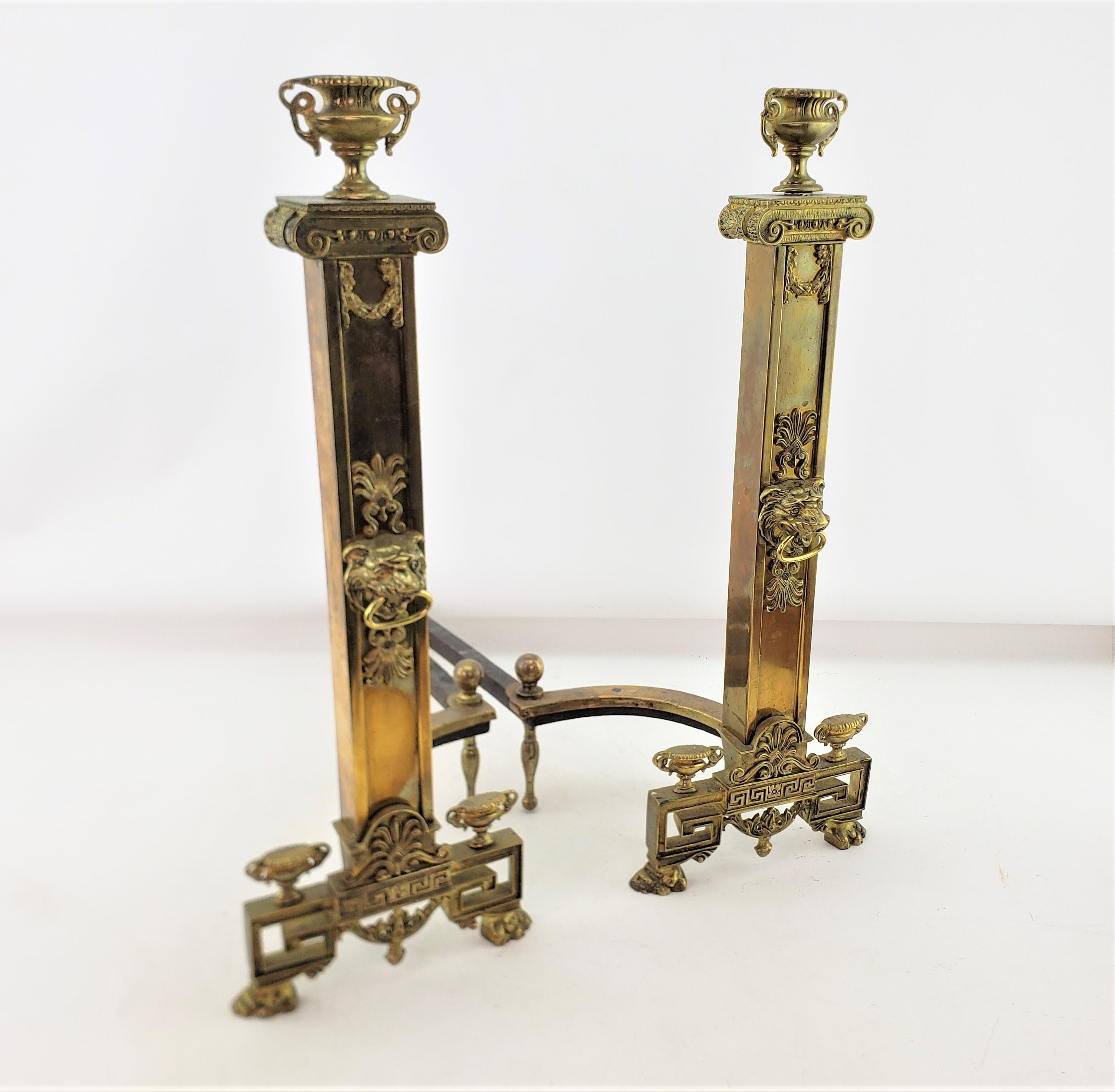 This pair of antique andirons are unsigned, but presumed to have originated from the United States and date to approximately 1900 and done in a Neoclassical Revival style. The andirons are composed of a cast and polished brass with cast iron