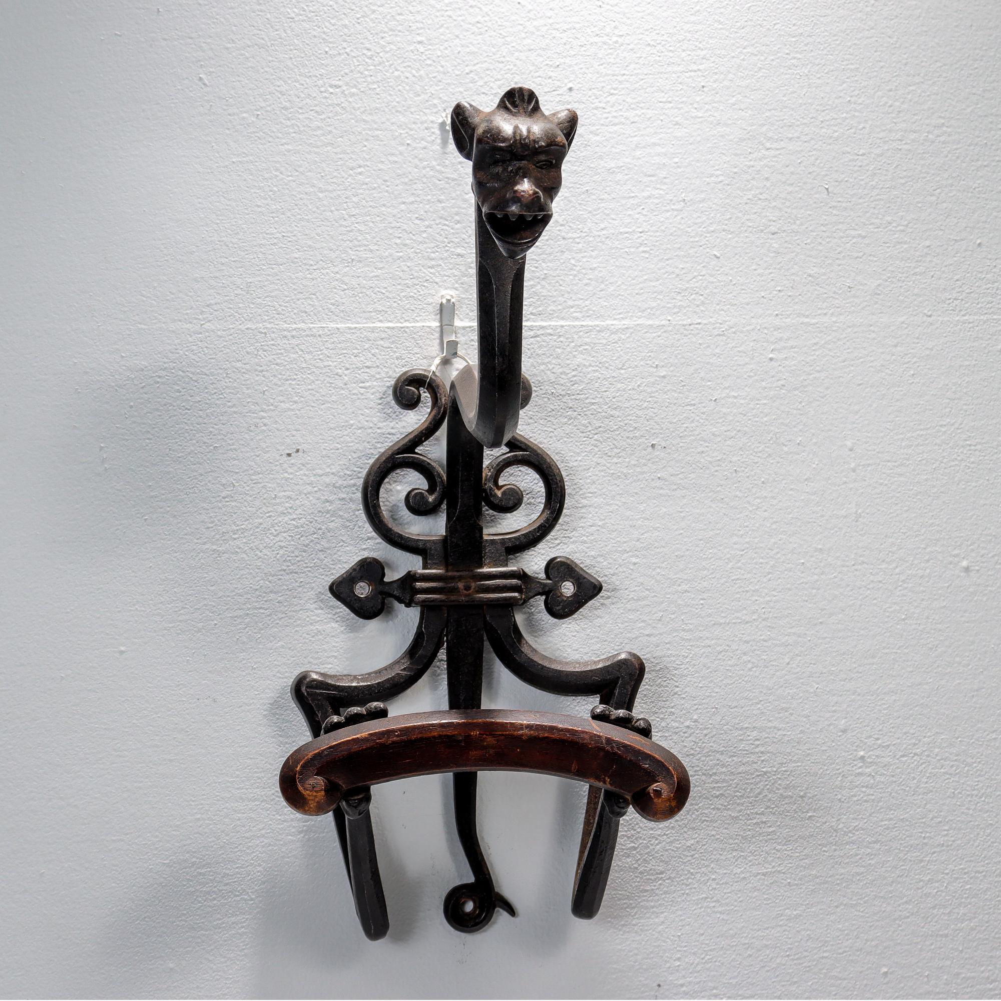 A fine antique Gothic Revival coat rack.

In the form of a two-legged gargoyle with an elongated neck holding a wooden support and mounted to the wall with a shaped bracket. 

In handmade wrought iron with a carved wooden support across the