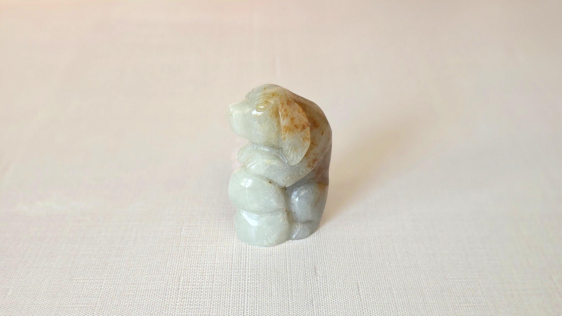 Ein niedlicher, handgeschnitzter Jagdhund aus feiner Nephrit-Jade, der mit den Vorderpfoten auf einem naturalistischen Felsen ruht und seinen Blick erwartungsvoll nach vorne richtet. Die ruhige Haltung und der aufmerksame Gesichtsausdruck der Figur